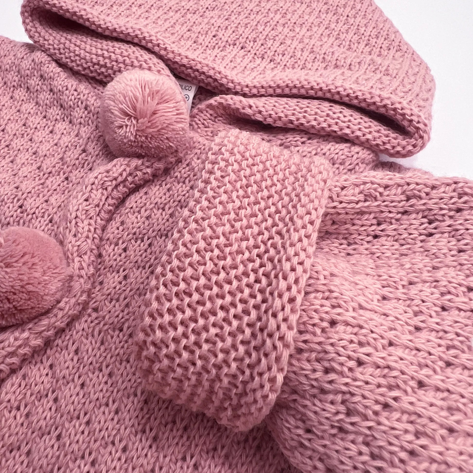Pormenor de casaco de malha com capuz com pompons na zona dos botões rosa