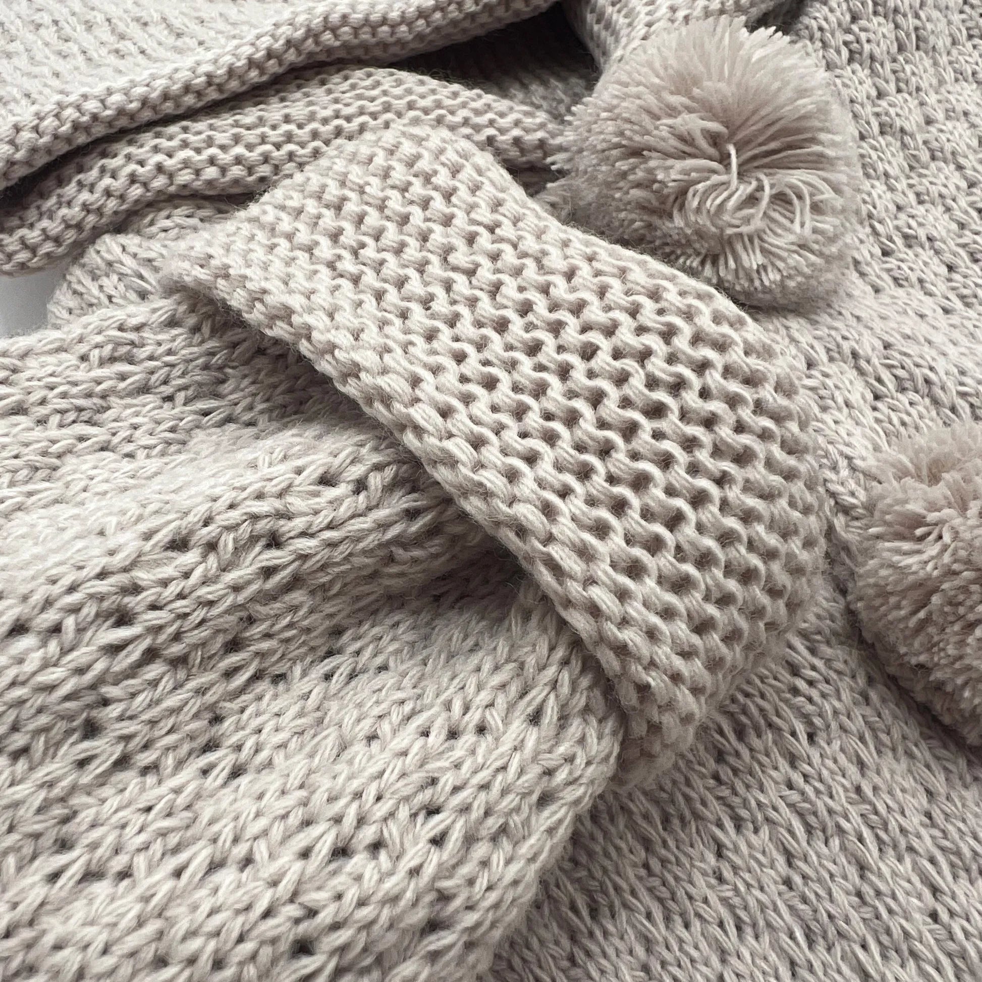 Pormenor de casaco de malha com capuz com pompons na zona dos botões taupe