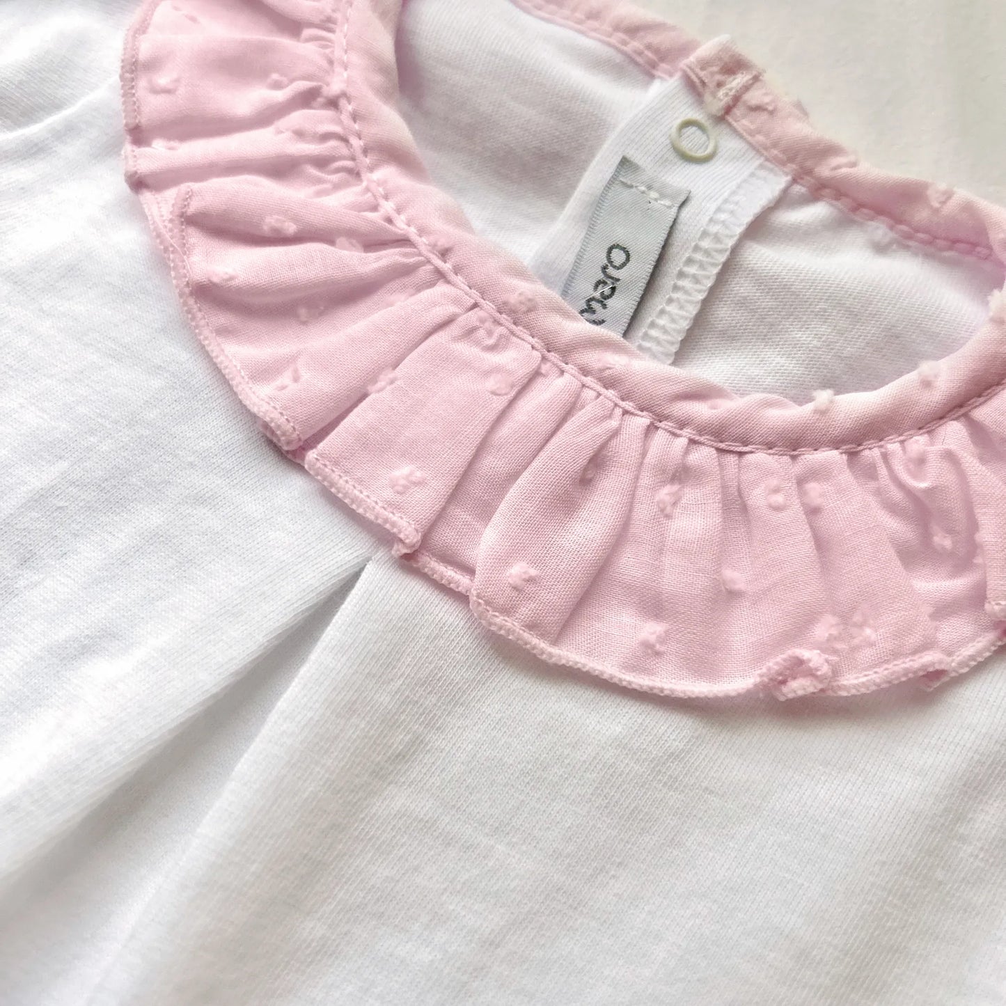 Pormenor de conjunto de menina de blusa com folho na gola e tapa-fraldas rosa