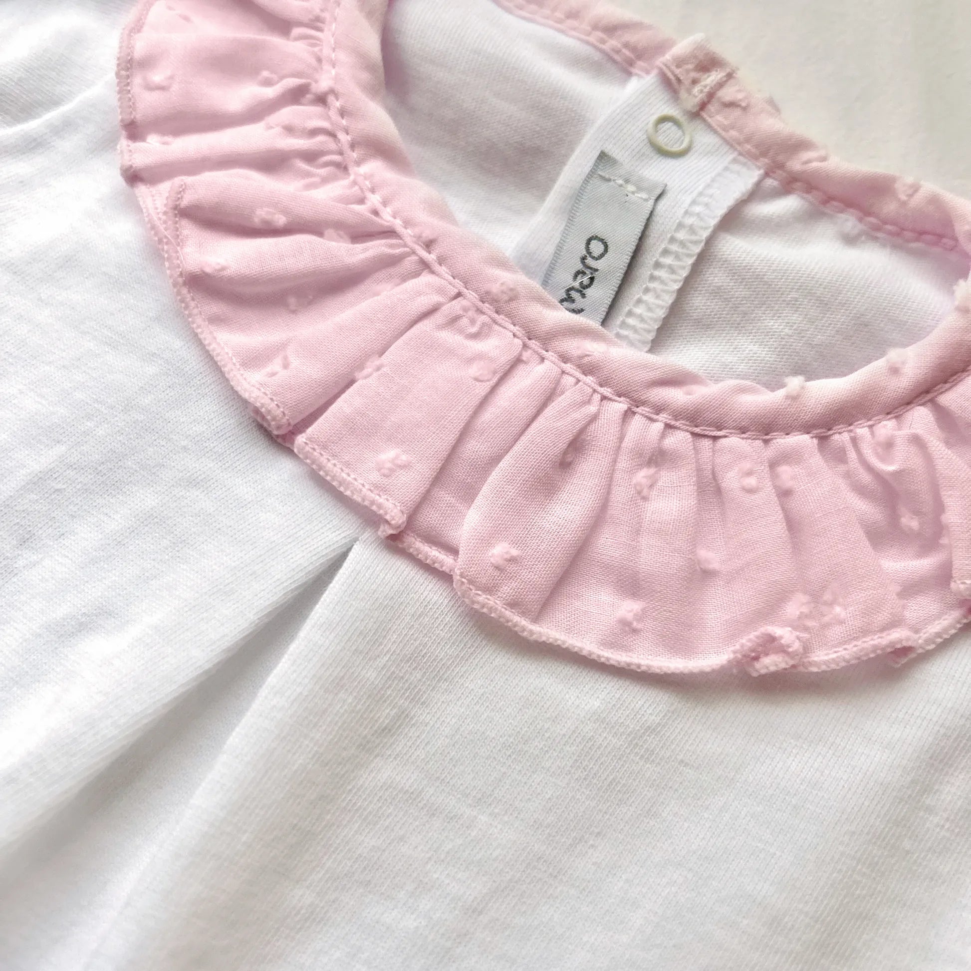 Pormenor de conjunto de menina de blusa com folho na gola e tapa-fraldas rosa