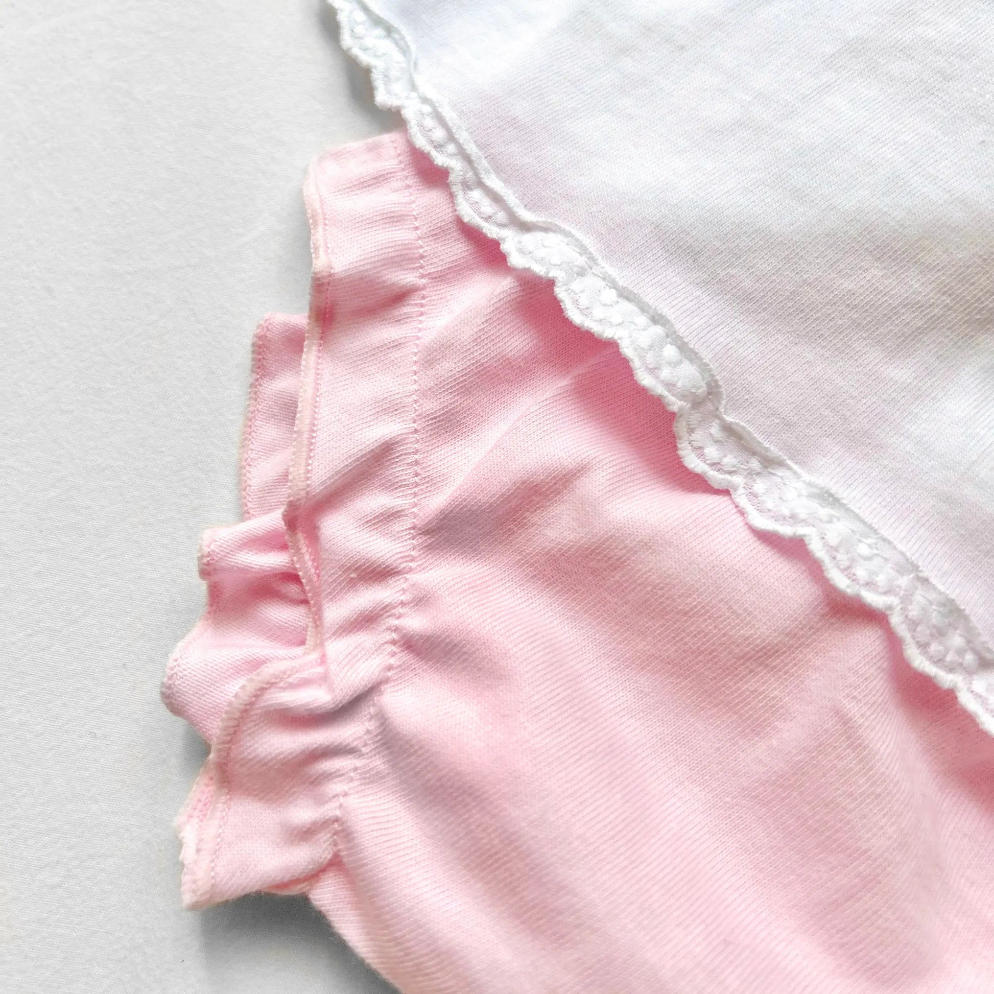 Pormenor de conjunto de menina de blusa com folho na gola e tapa-fraldas rosa