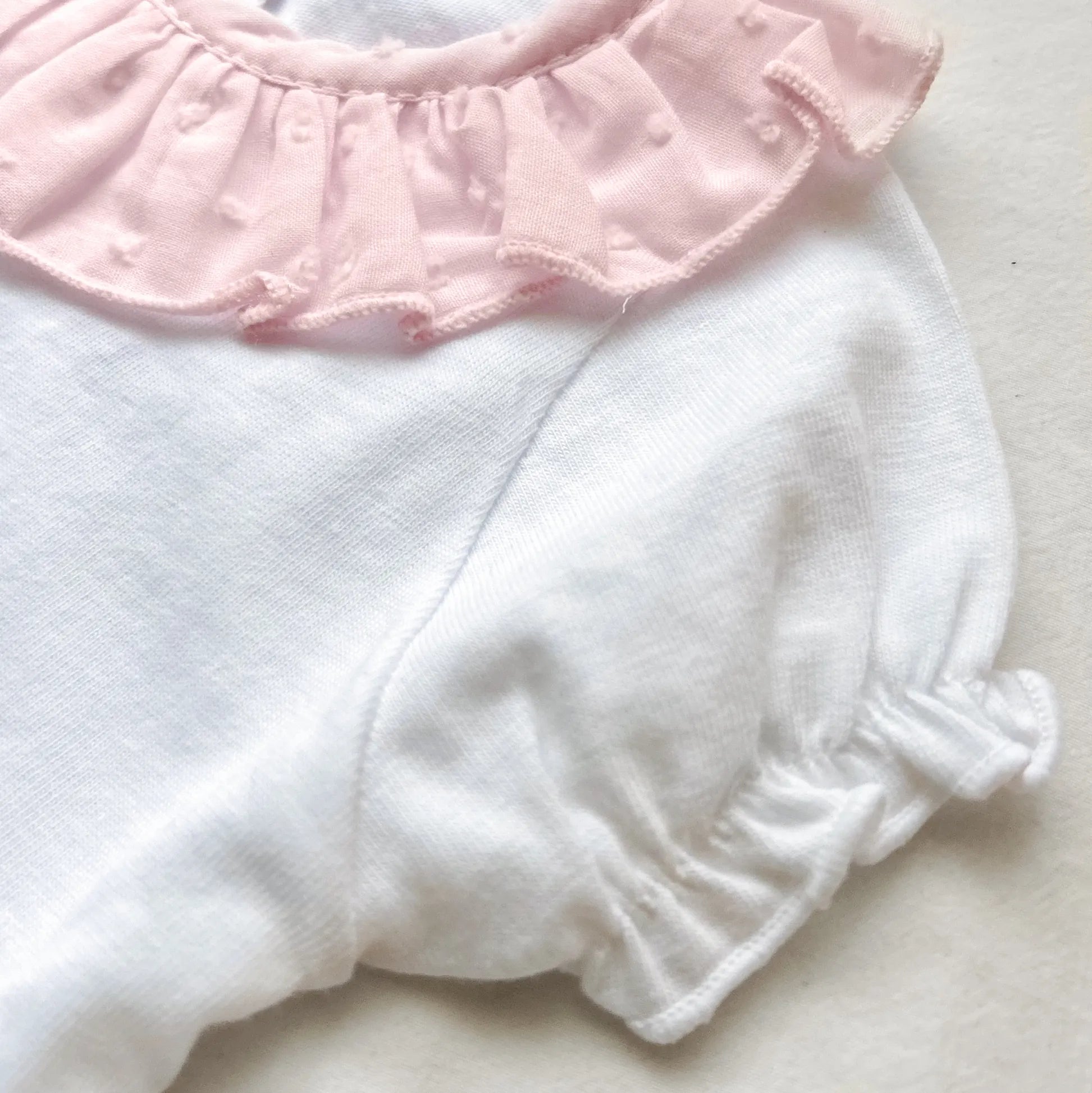 Pormenor de conjunto de menina de blusa com folho na gola e tapa-fraldas rosa
