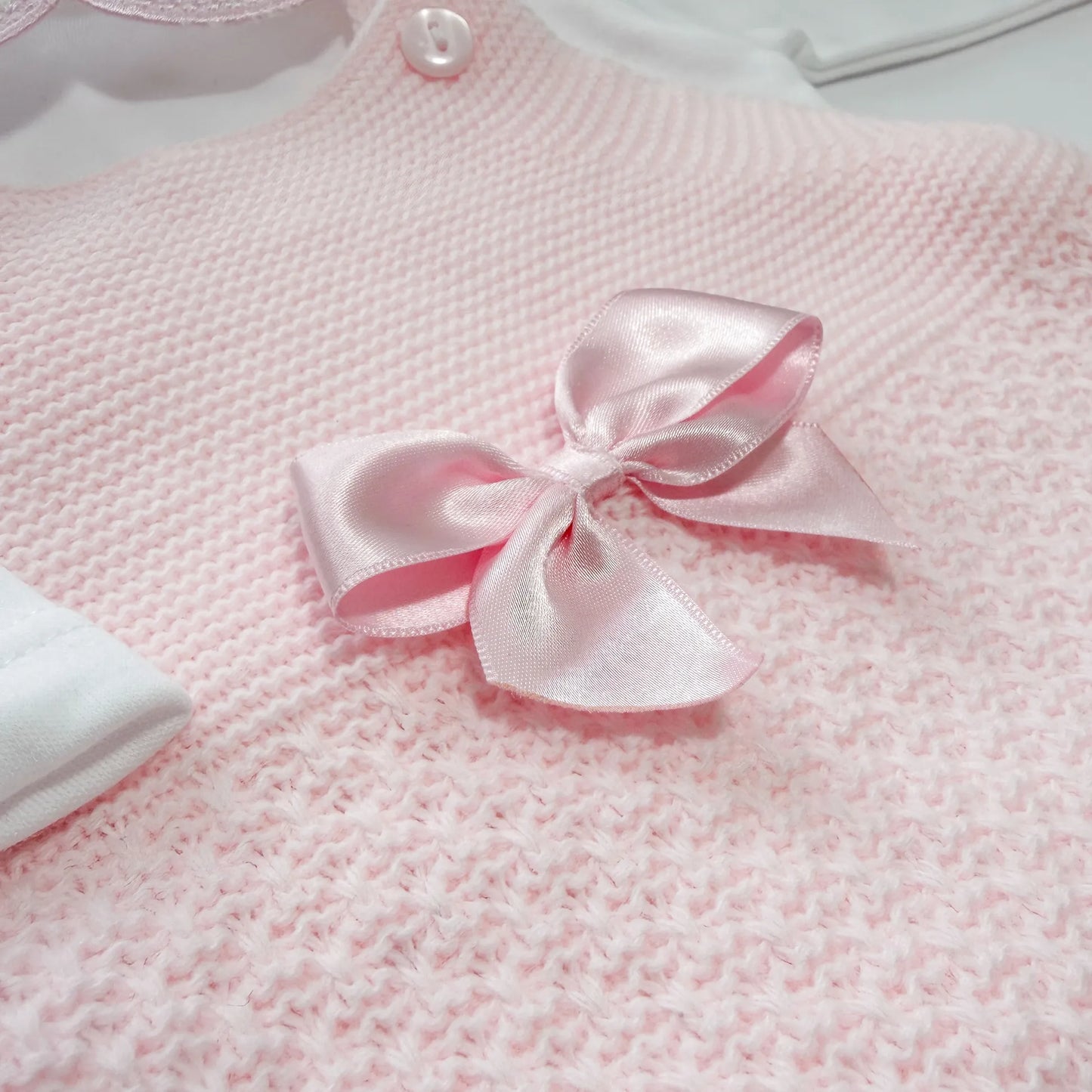 Detalhe de conjunto de menina de jardineira com laço, camisola e gorro com pompom em tricot rosa