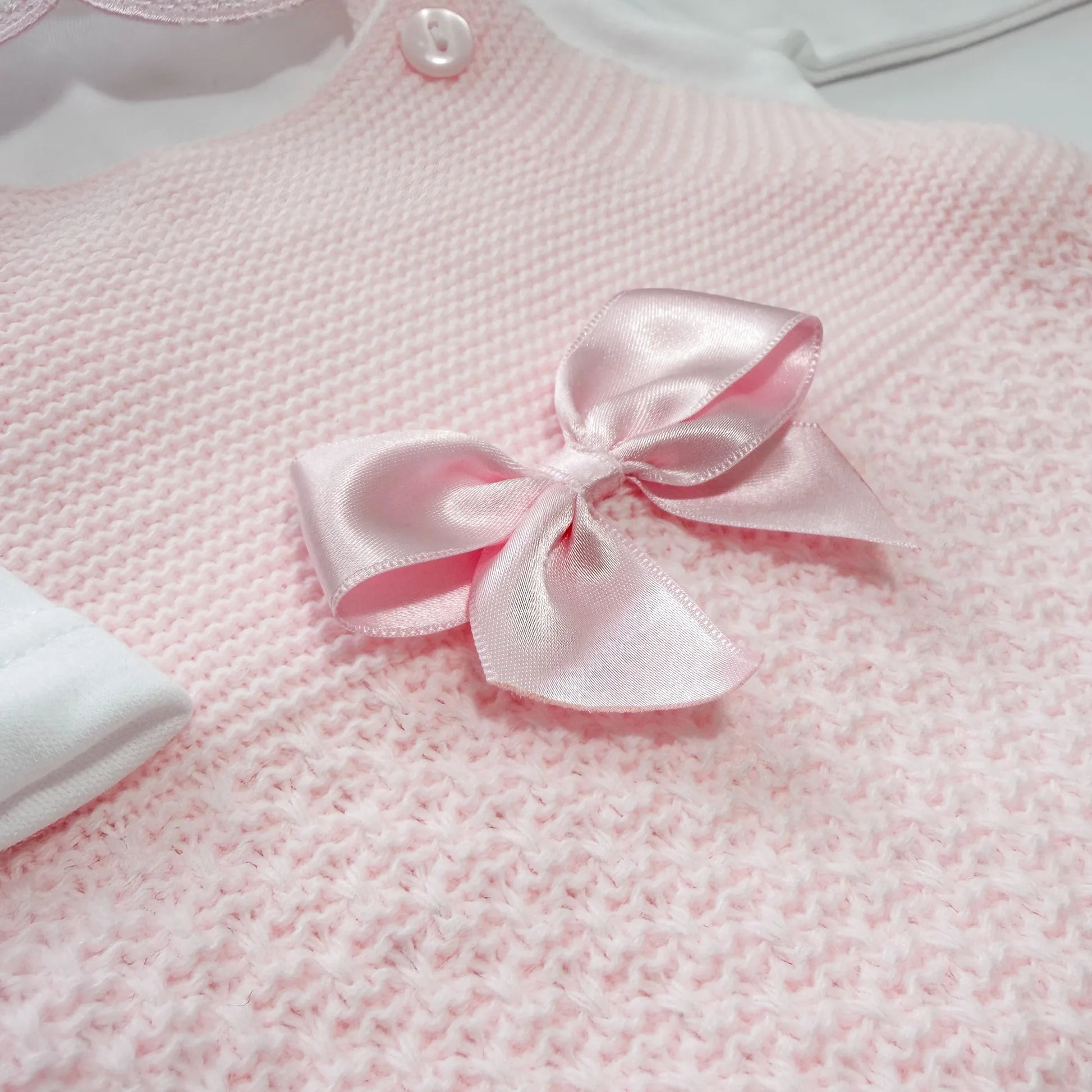 Detalhe de conjunto de menina de jardineira com laço, camisola e gorro com pompom em tricot rosa