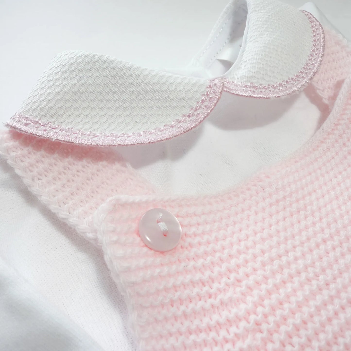 Detalhe de conjunto de menina de jardineira com laço, camisola e gorro com pompom em tricot rosa