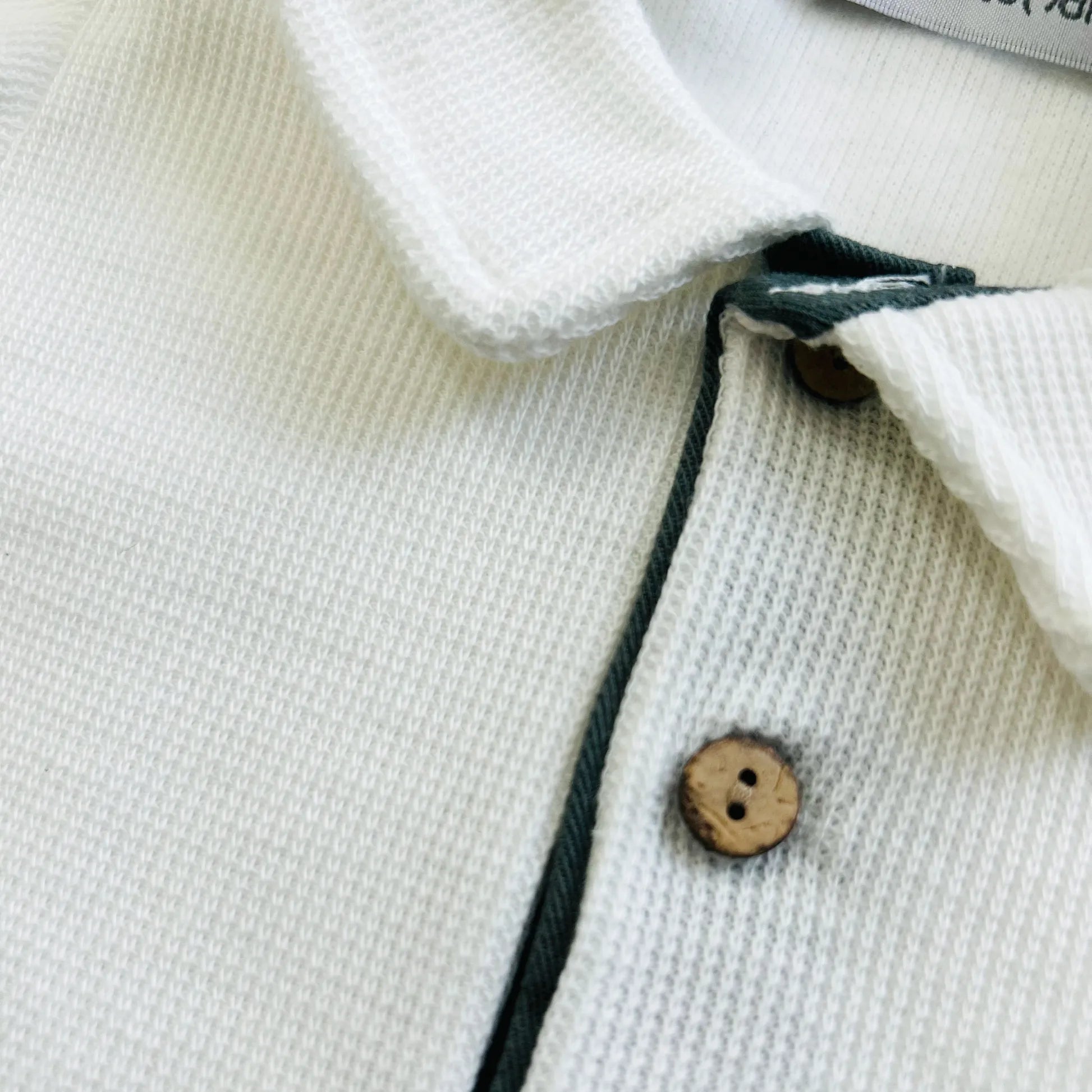 Pormenor de conjunto de menino de camisola cru com botões e calção de tecido verde