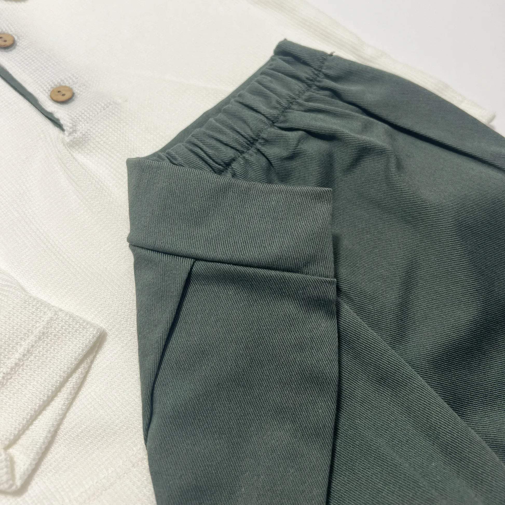 Pormenor de conjunto de menino de camisola cru com botões e calção de tecido verde