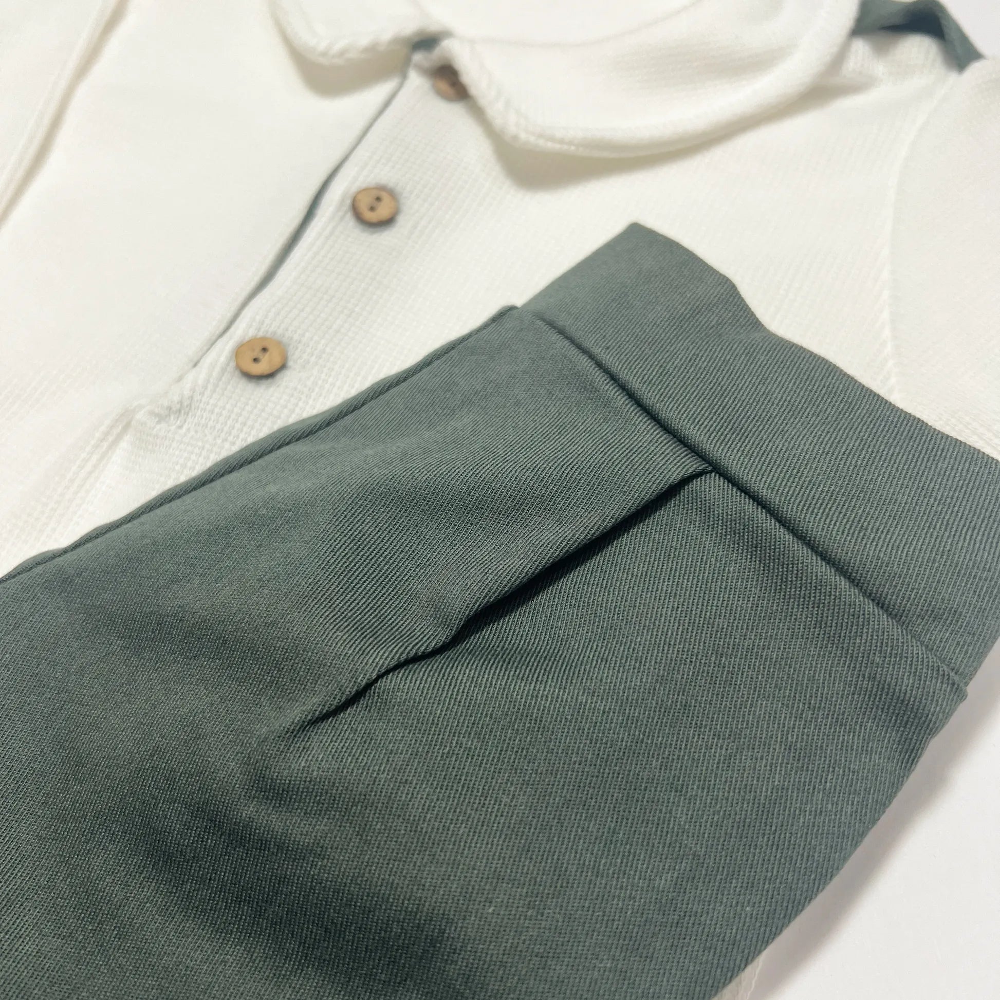 Pormenor de conjunto de menino de camisola cru com botões e calção de tecido verde