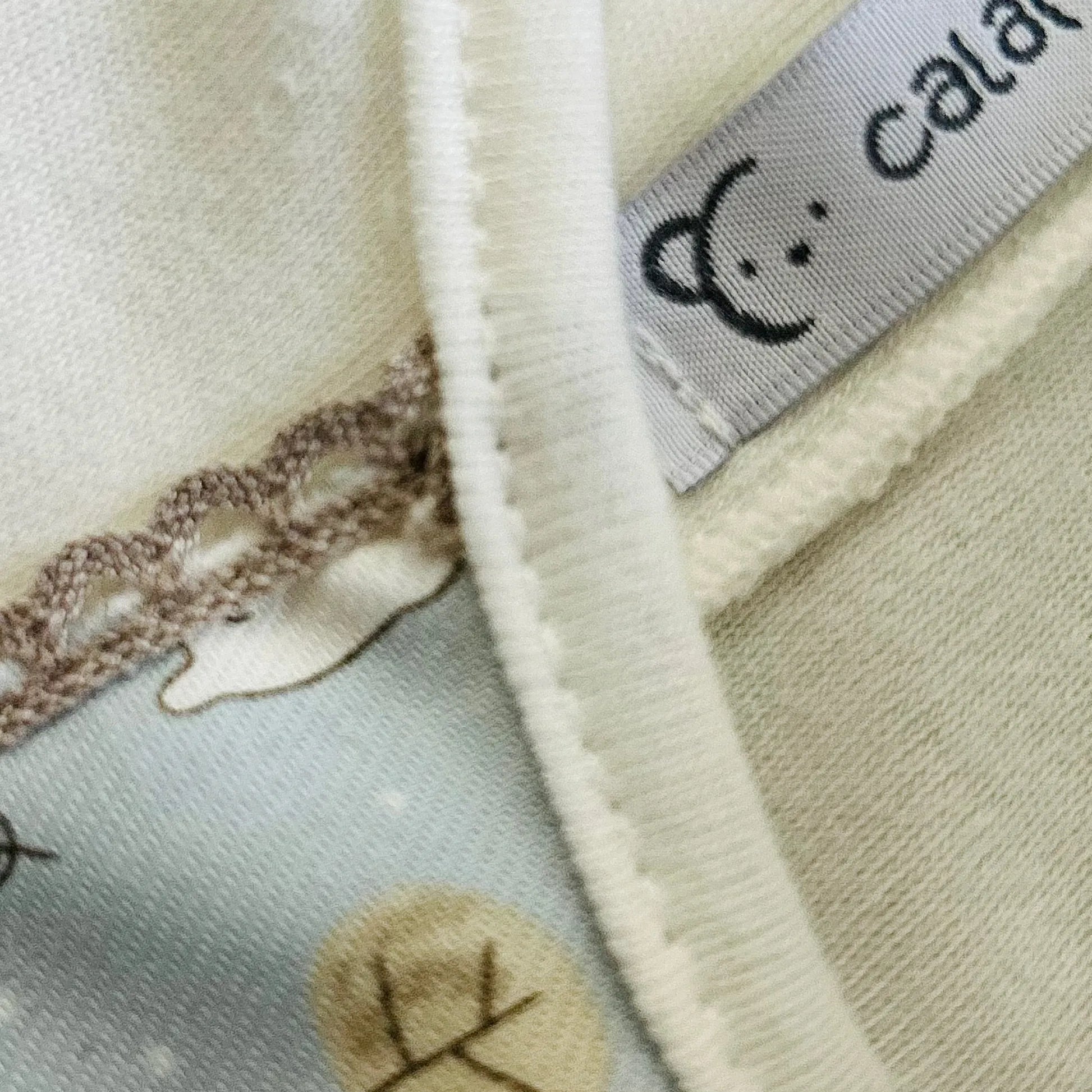 Pormenor de conjunto de menino de camisola branca com faixa decorativa e tapa-fraldas cinza