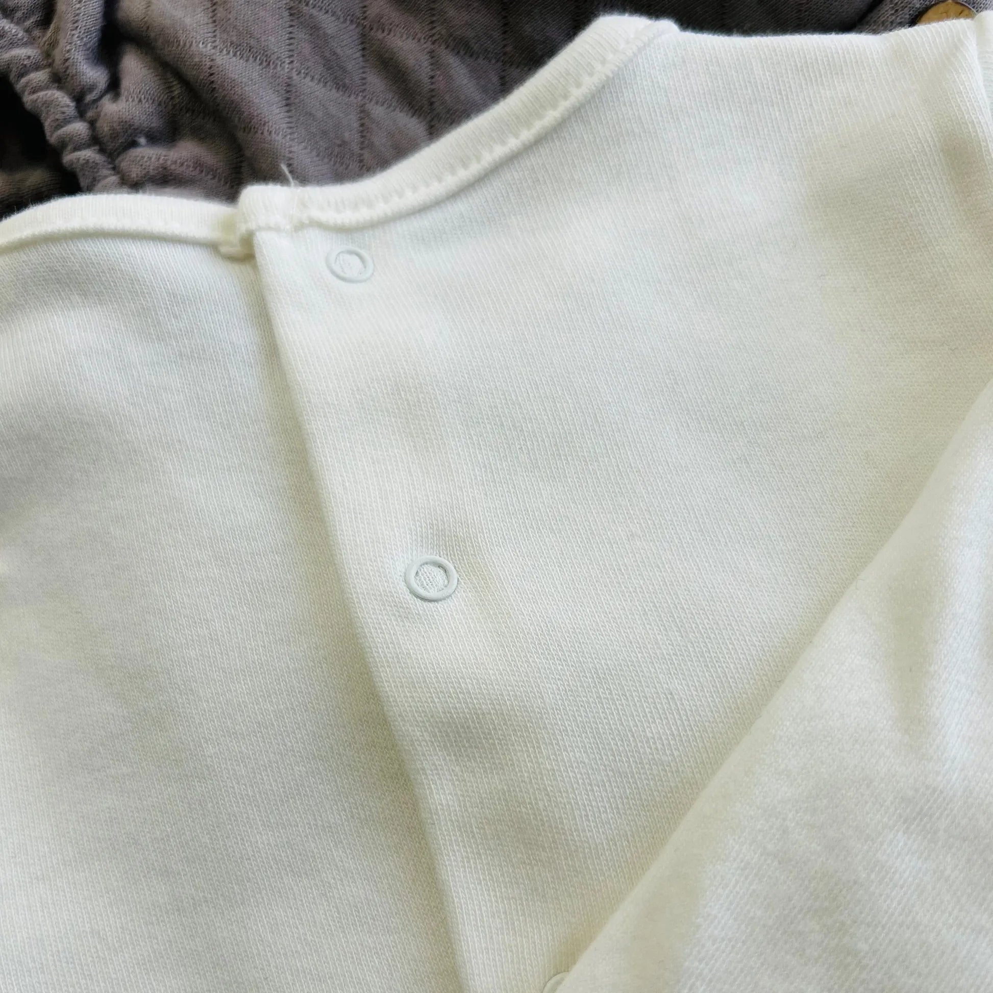 Pormenor de conjunto de menino de camisola branca com faixa decorativa e tapa-fraldas cinza
