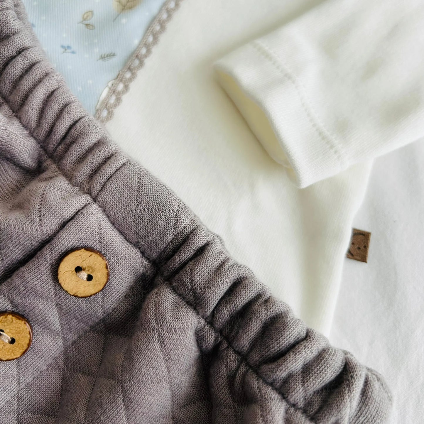 Pormenor de conjunto de menino de camisola branca com faixa decorativa e tapa-fraldas cinza