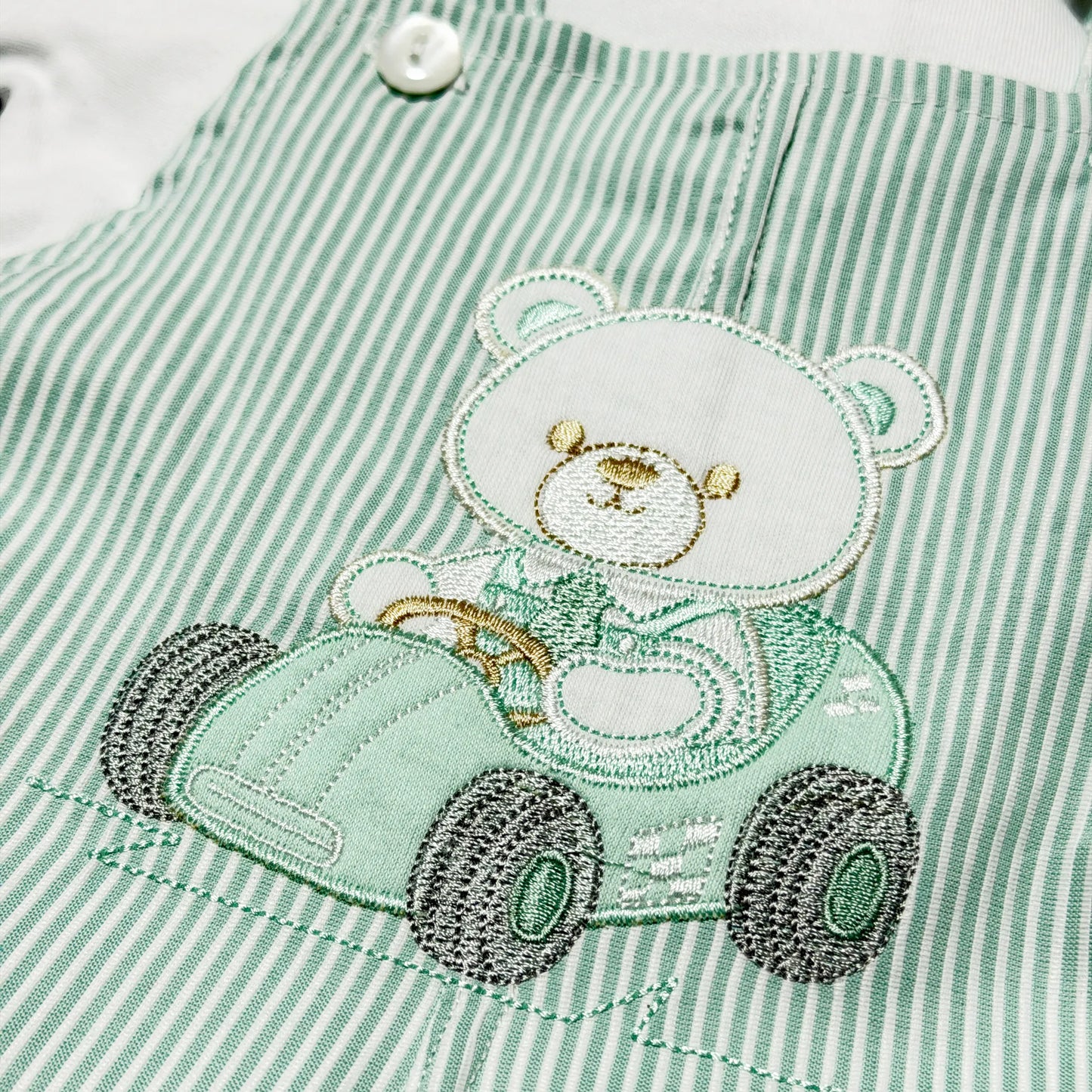 Detalhe de conjunto de menino de jardineira às riscas com motivo bordado de ursinho verde