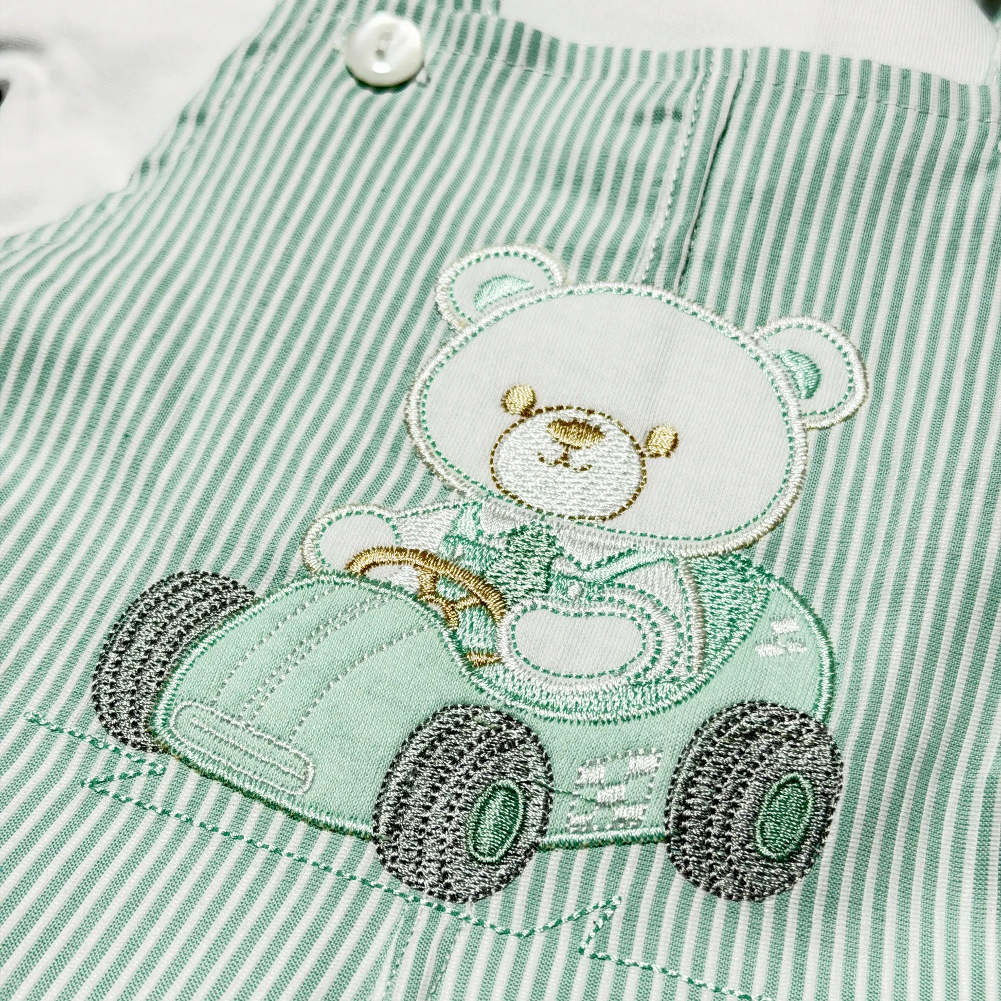 Detalhe de conjunto de menino de jardineira às riscas com motivo bordado de ursinho verde