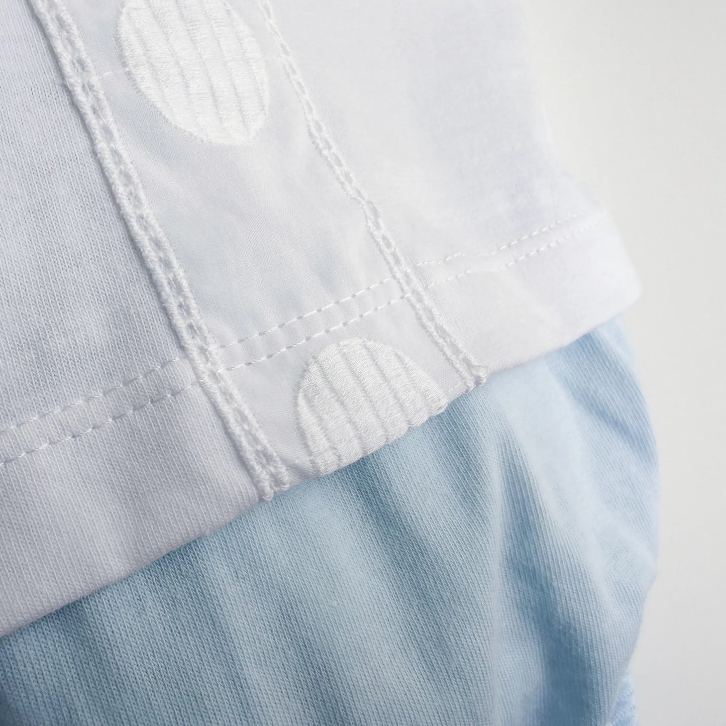 Pormenor de conjunto de menino de T-shirt com faixa decorativa bordada e tapa-fraldas azul