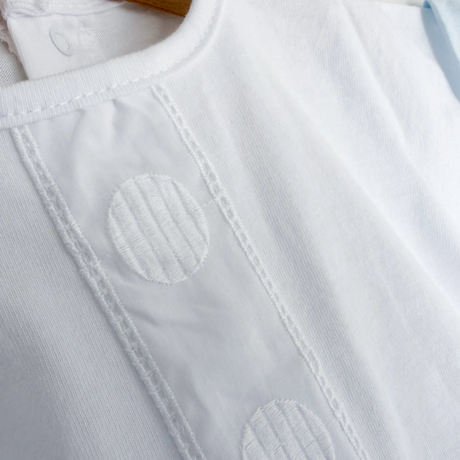 Pormenor de conjunto de menino de T-shirt com faixa decorativa bordada e tapa-fraldas azul