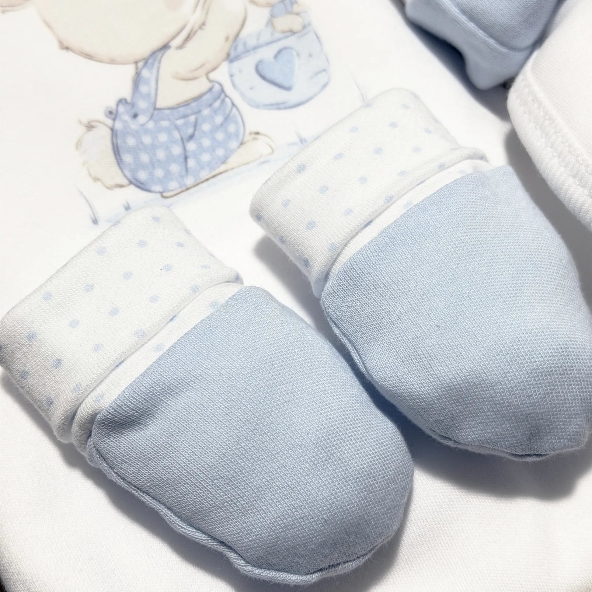 Pormenor de conjunto de primeira roupinha com motivo coelhinho na cesta azul