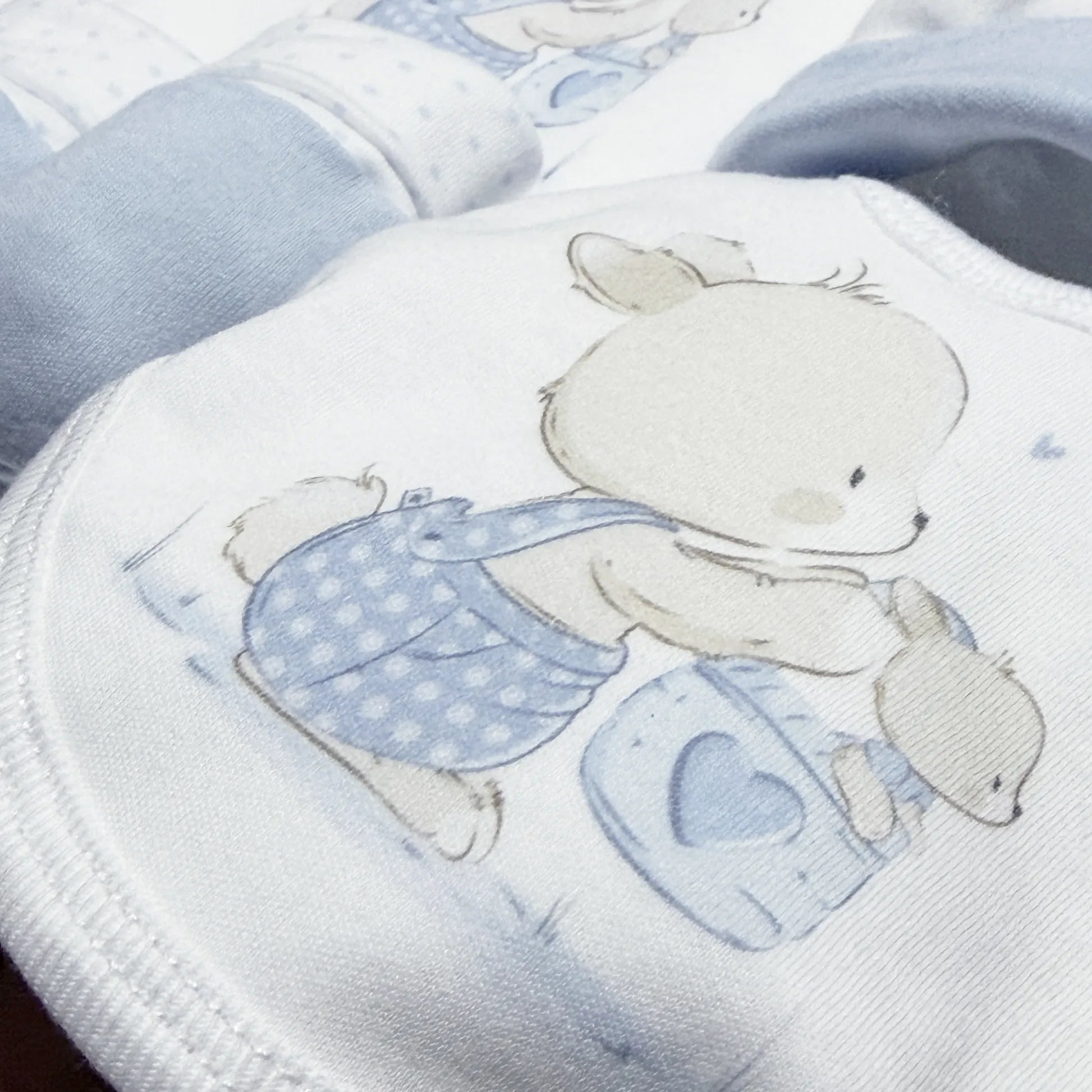 Pormenor de conjunto de primeira roupinha com motivo coelhinho na cesta azul