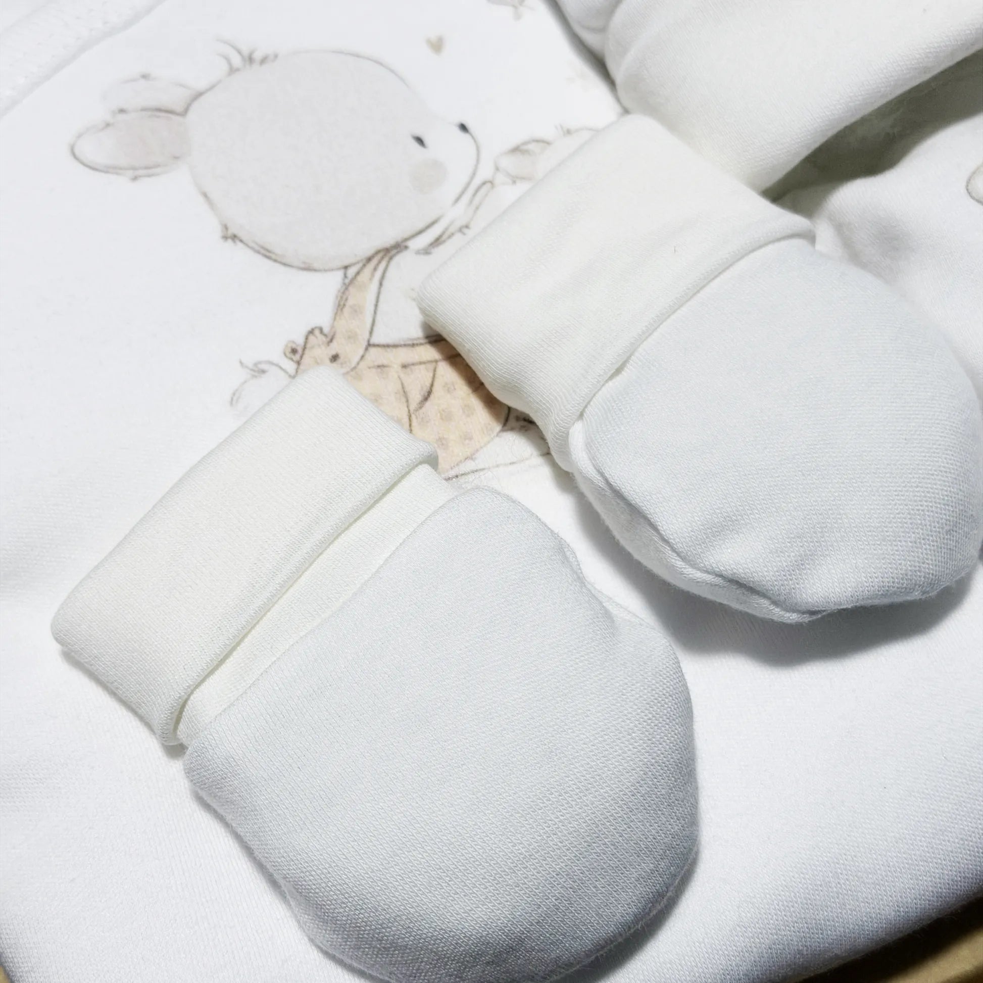 Pormenor de conjunto de primeira roupinha com motivo coelhinho na cesta bege