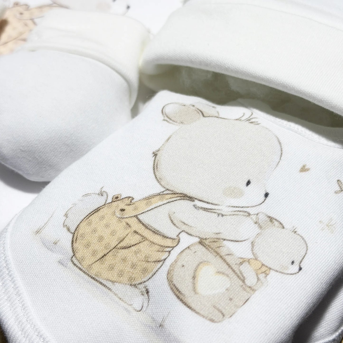 Pormenor de conjunto de primeira roupinha com motivo coelhinho na cesta bege