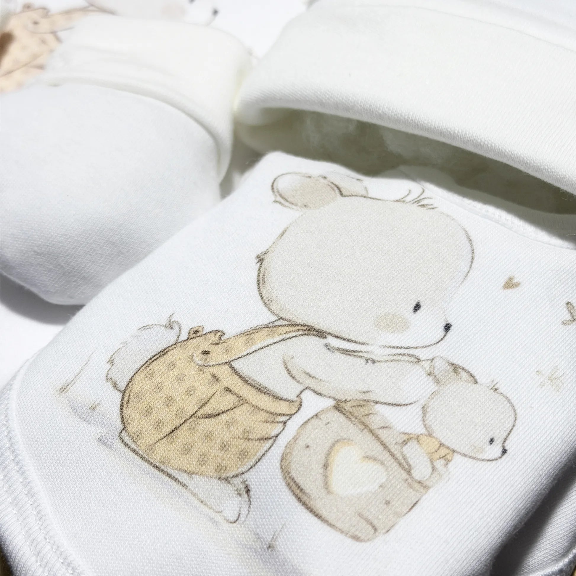 Pormenor de conjunto de primeira roupinha com motivo coelhinho na cesta bege