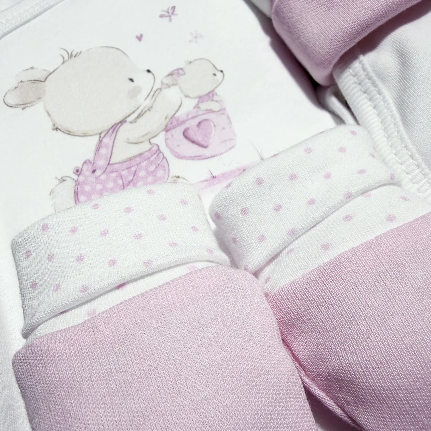 Pormenor de conjunto de primeira roupinha com motivo coelhinho na cesta rosa