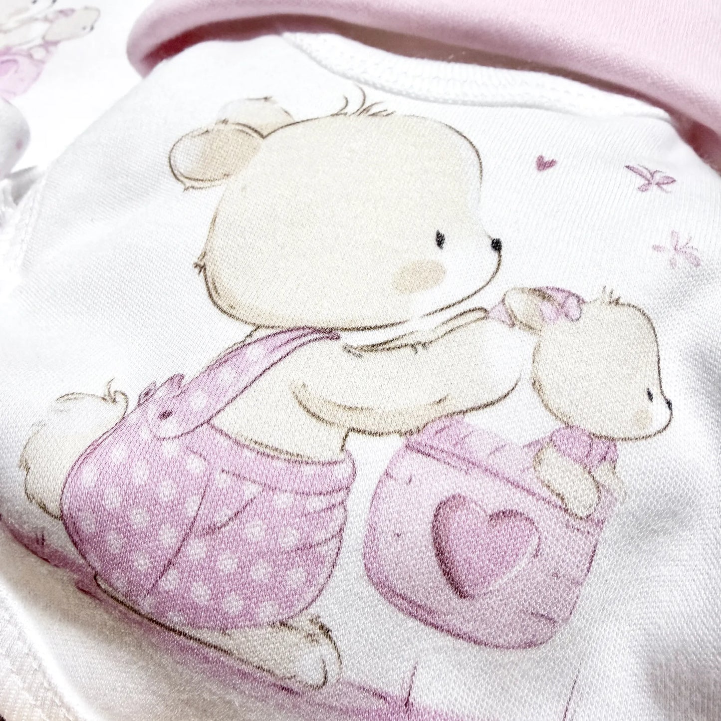 Pormenor de conjunto de primeira roupinha com motivo coelhinho na cesta rosa