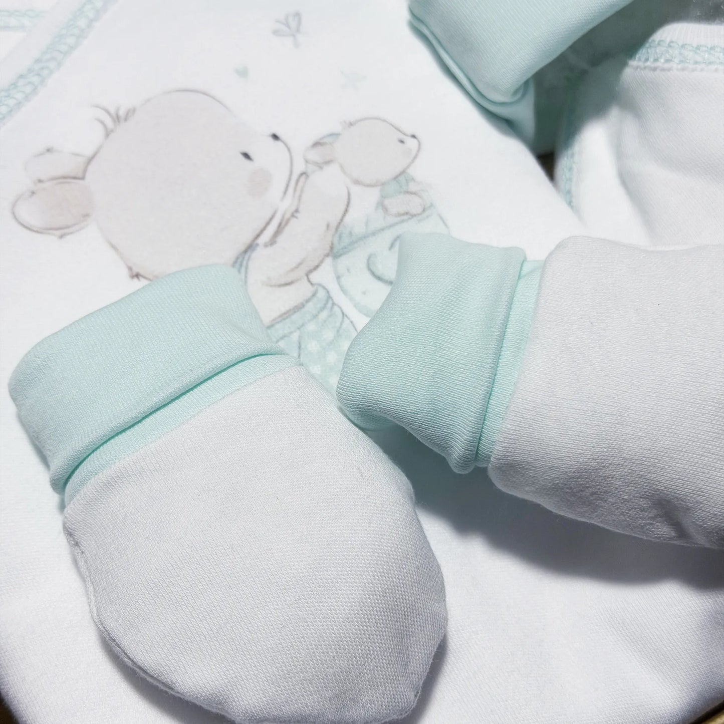 Pormenor de conjunto de primeira roupinha com motivo coelhinho na cesta verde