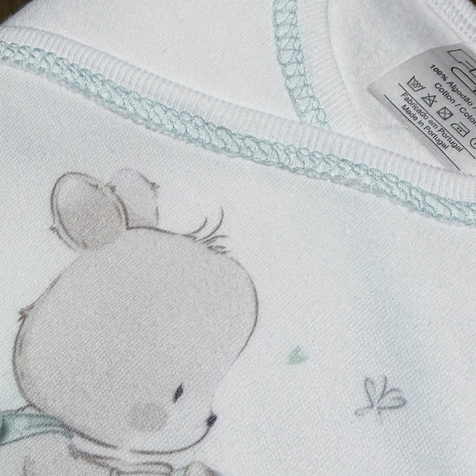 Pormenor de conjunto de primeira roupinha com motivo coelhinho na cesta verde