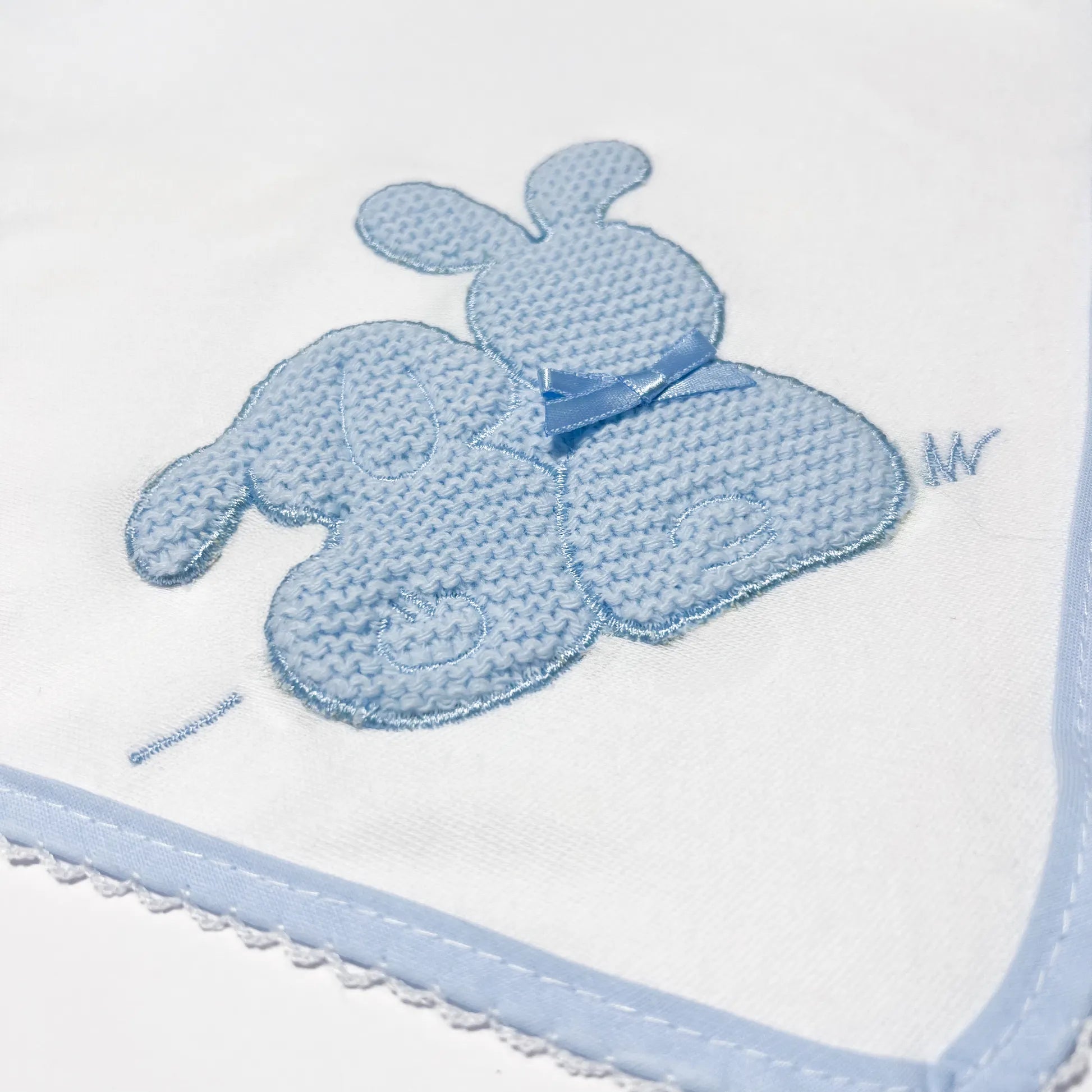 Pormenor de fralda com motivo coelhos tricot com lacinho azul