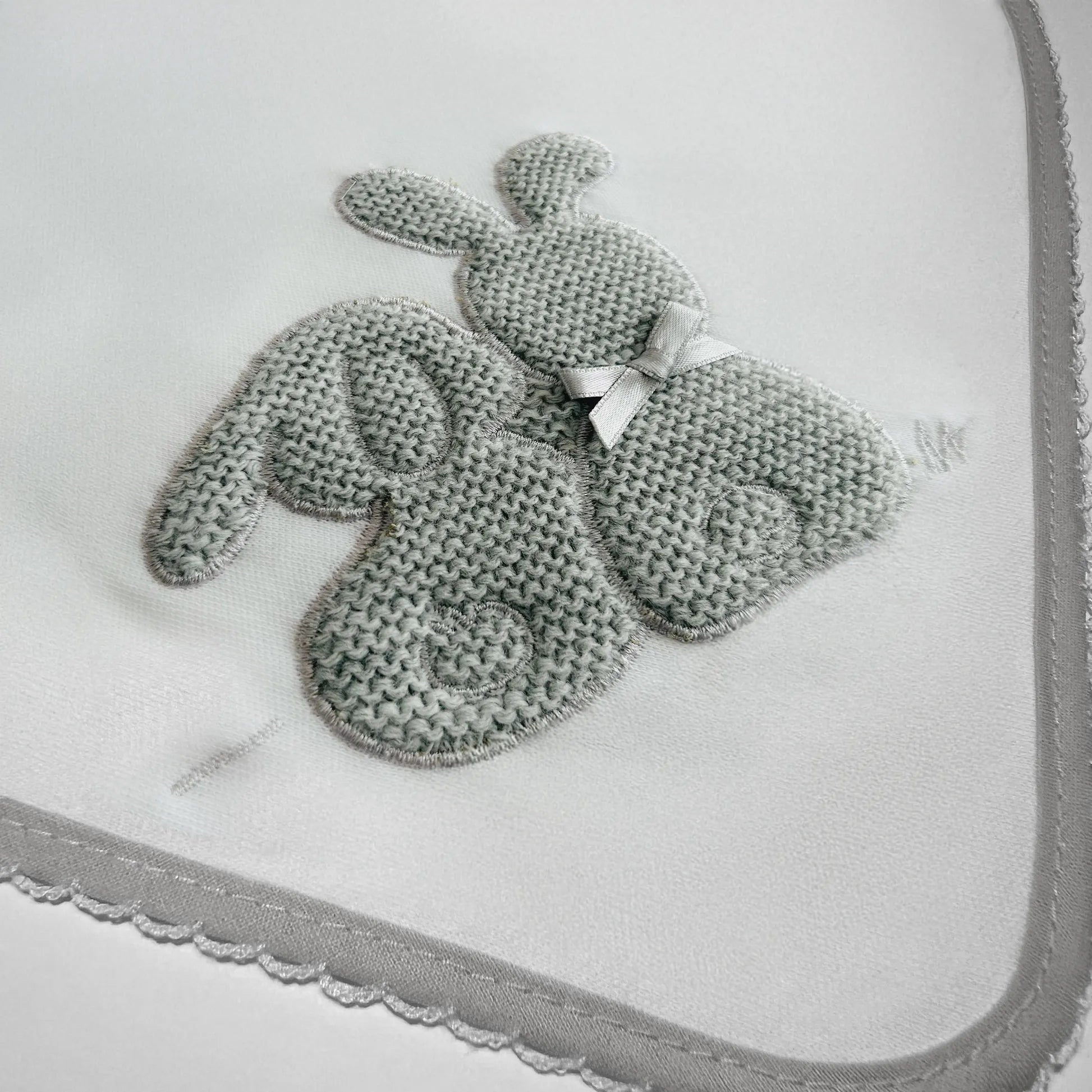 Pormenor de fralda com motivo coelhos tricot com lacinho cinza