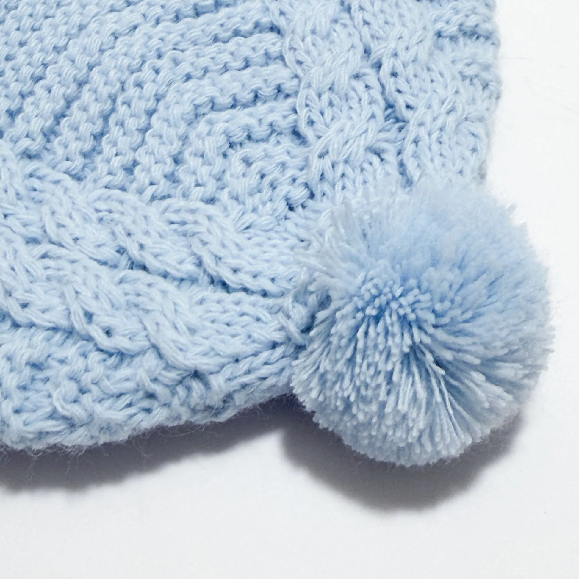Pormenor de gorro de malha tricotada com pompom azul