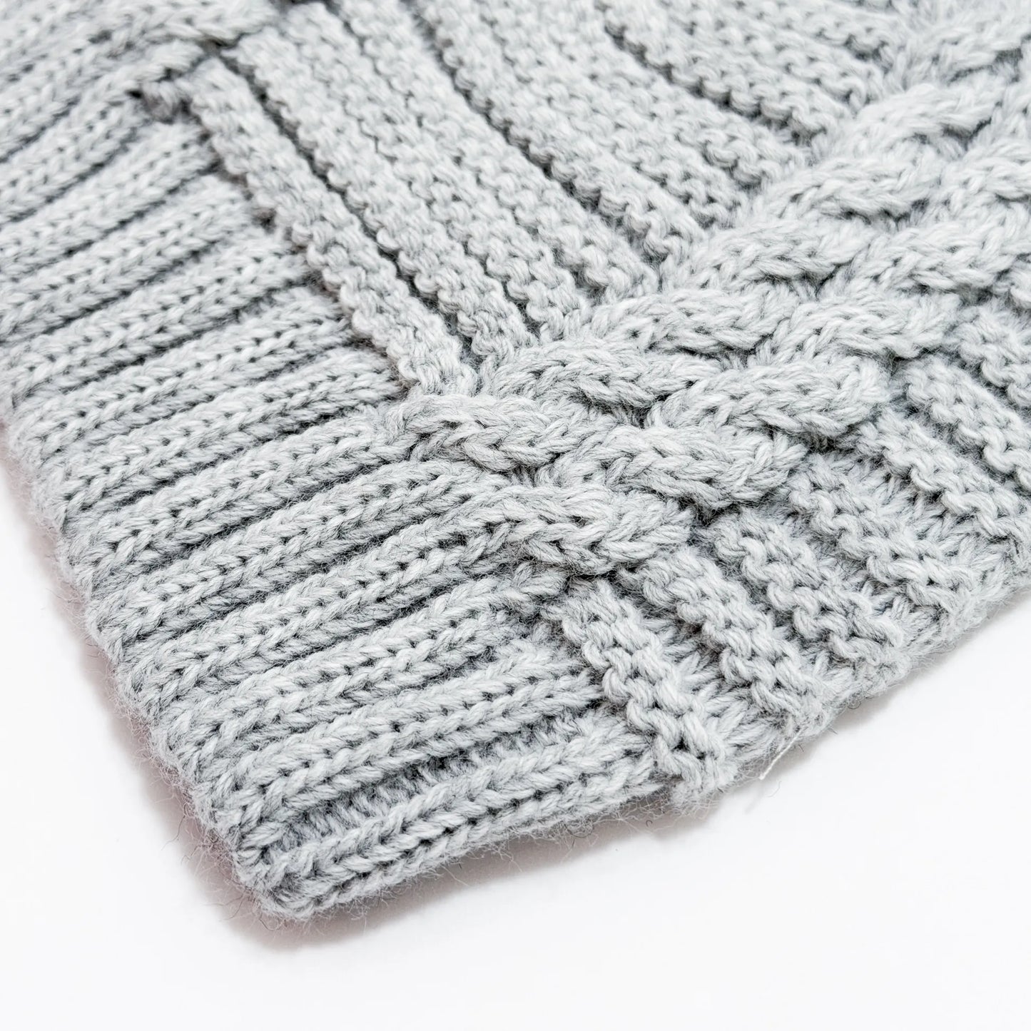 Pormenor de gorro de malha tricotada com pompom cinza