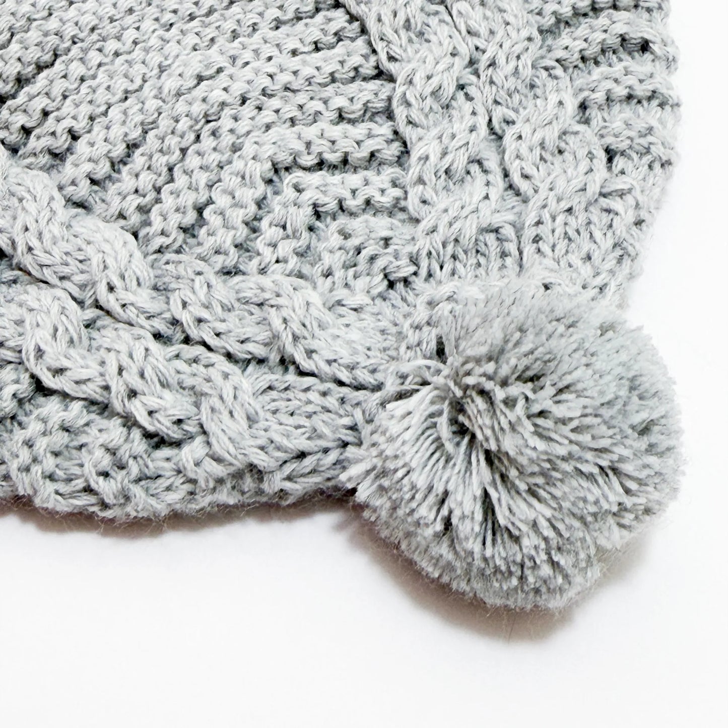 Pormenor de gorro de malha tricotada com pompom cinza