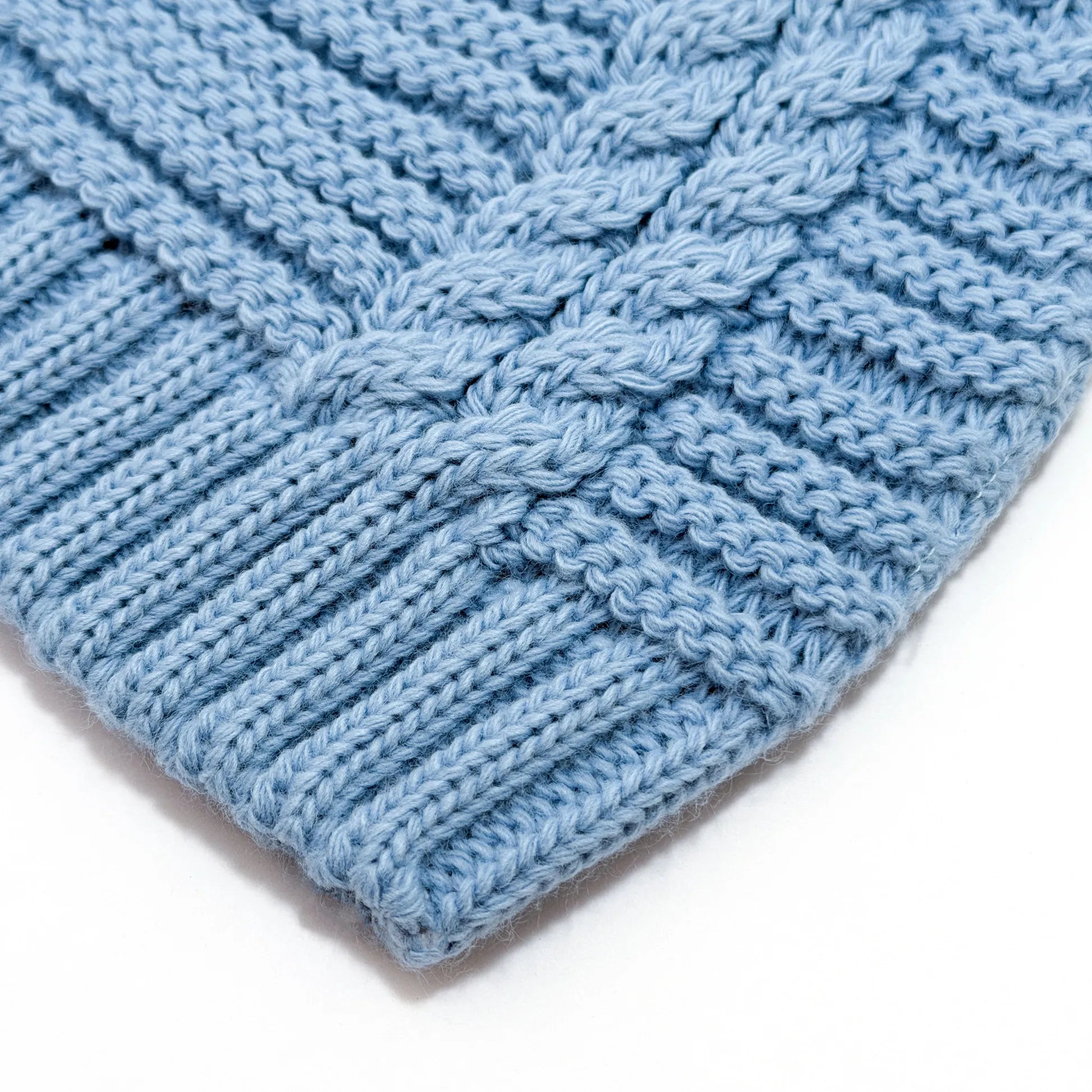Pormenor de gorro de malha tricotada com pompom cobalto