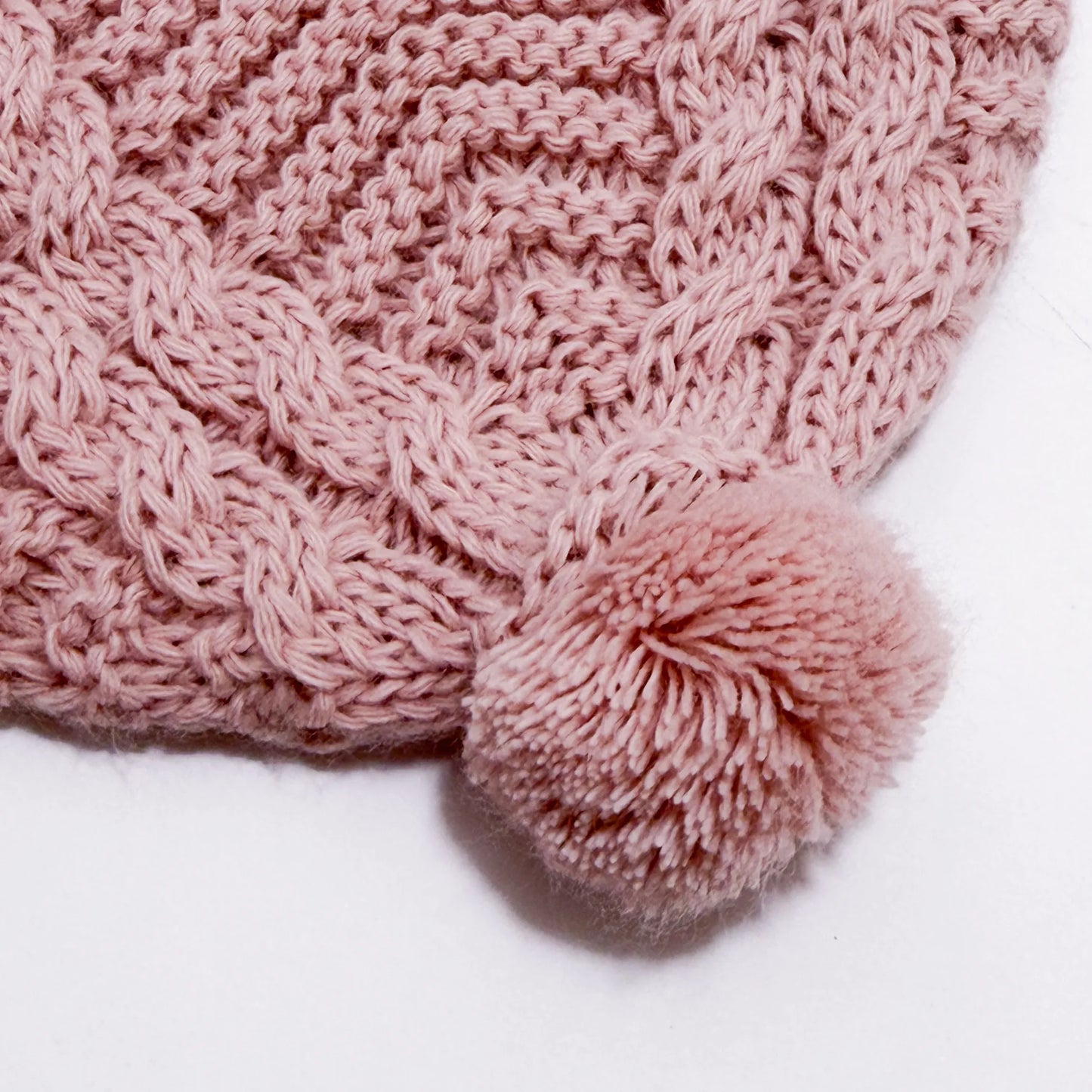 Pormenor de gorro de malha tricotada com pompom rosa
