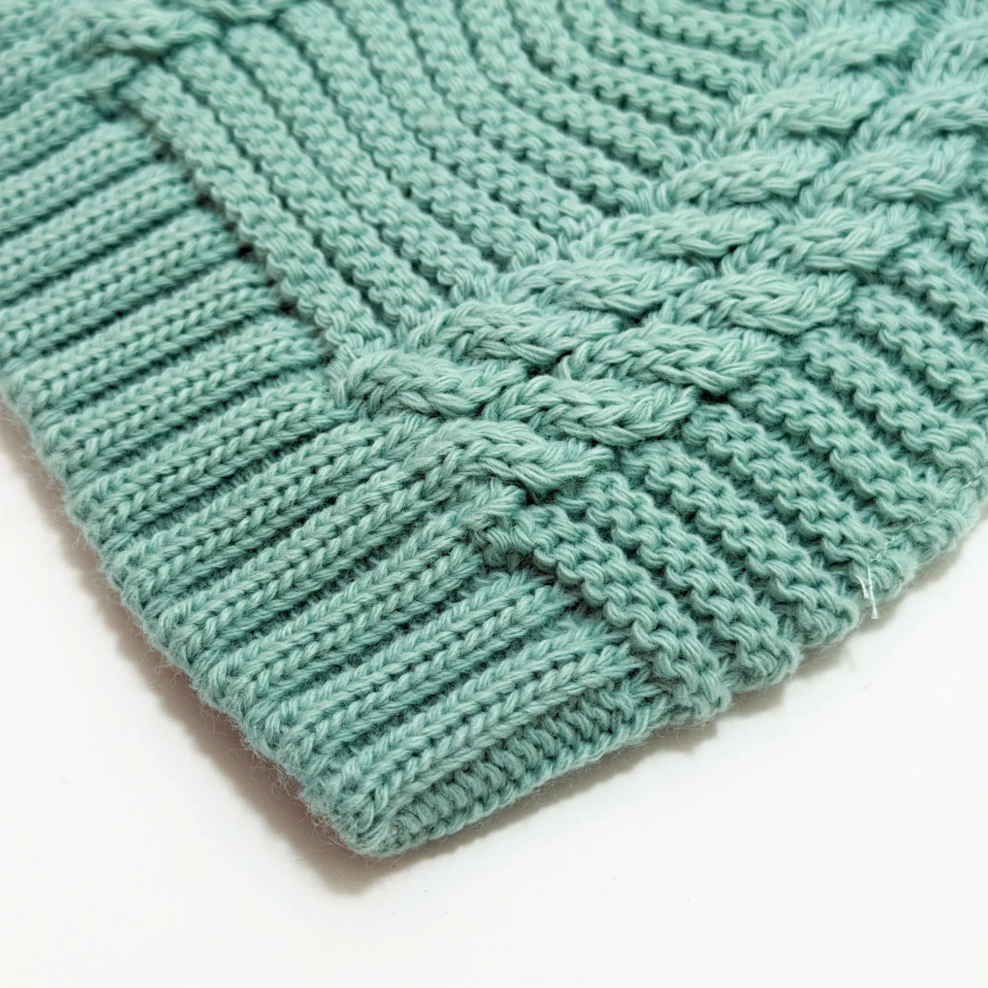 Pormenor de gorro de malha tricotada com pompom verde