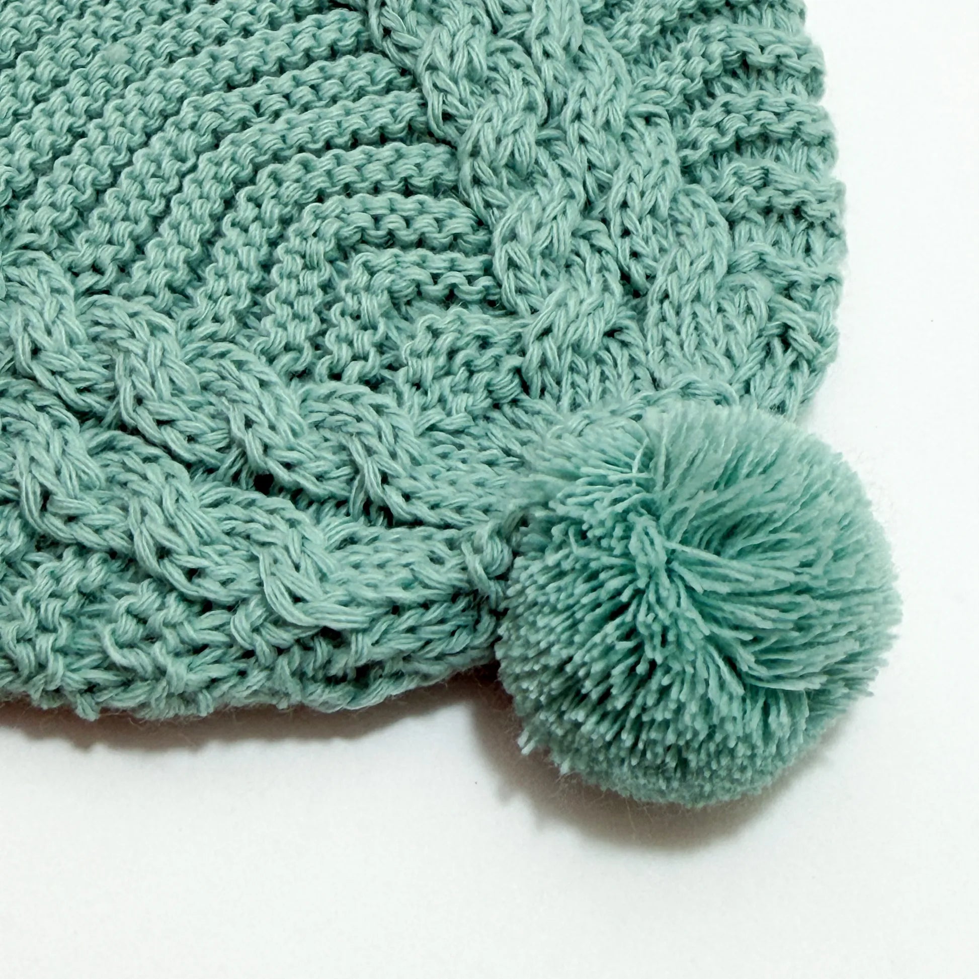 Pormenor de gorro de malha tricotada com pompom verde