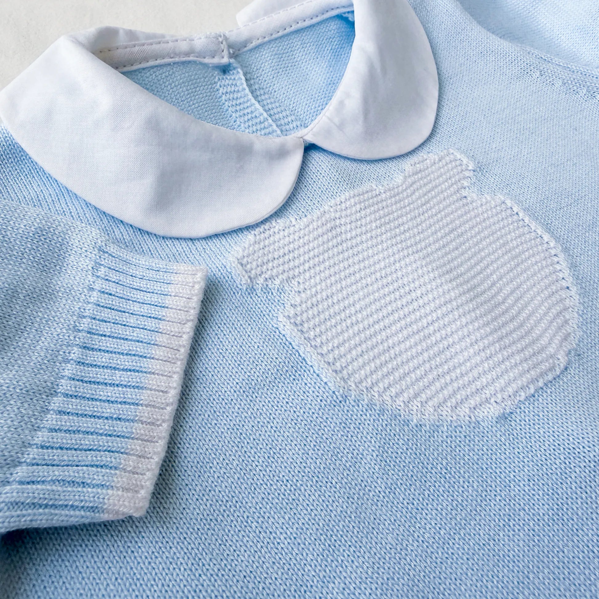 Pormenor de macacão em malha com gola Peter Pan e motivo ursinho azul