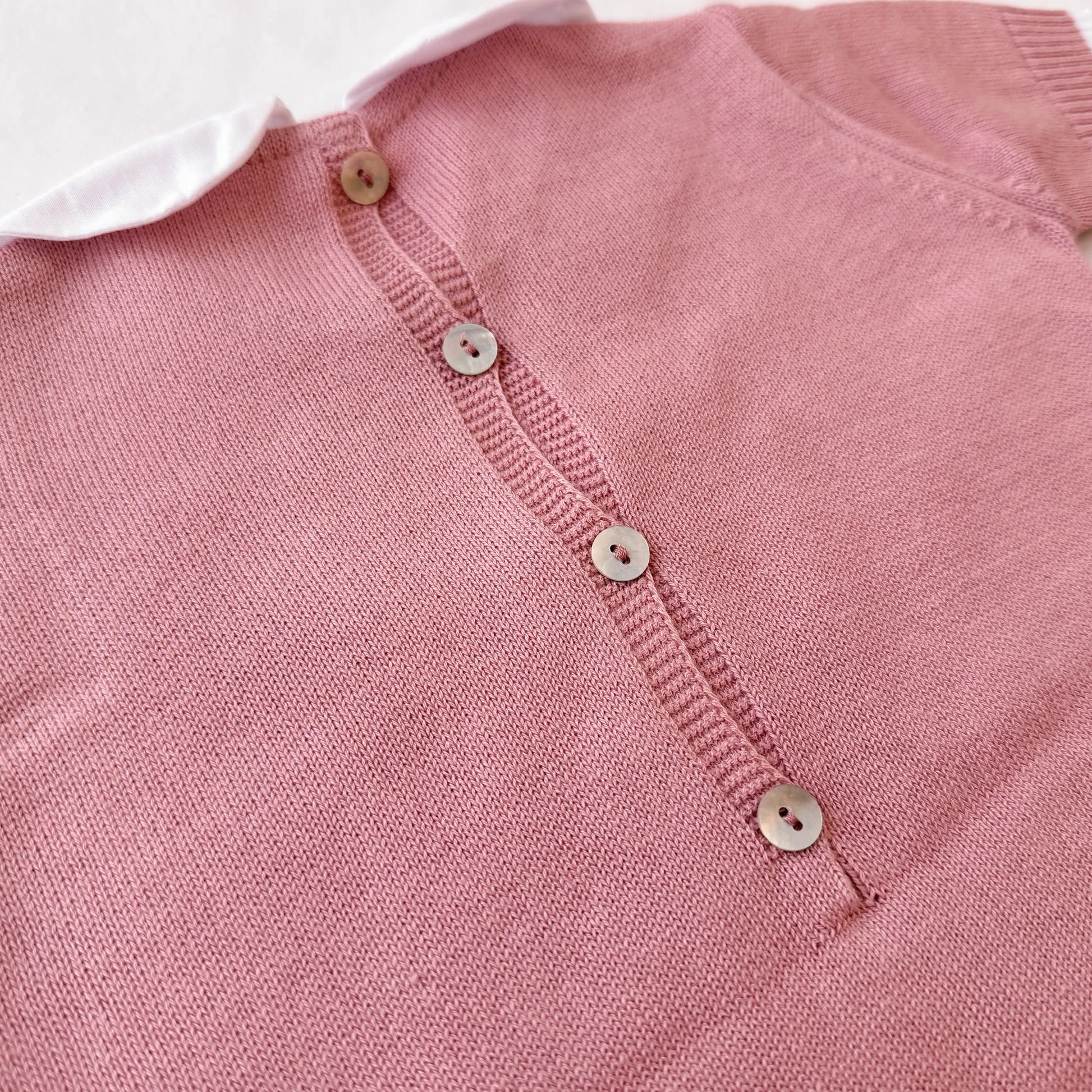 Pormenor de macacão em malha com gola Peter Pan e motivo ursinho rosa