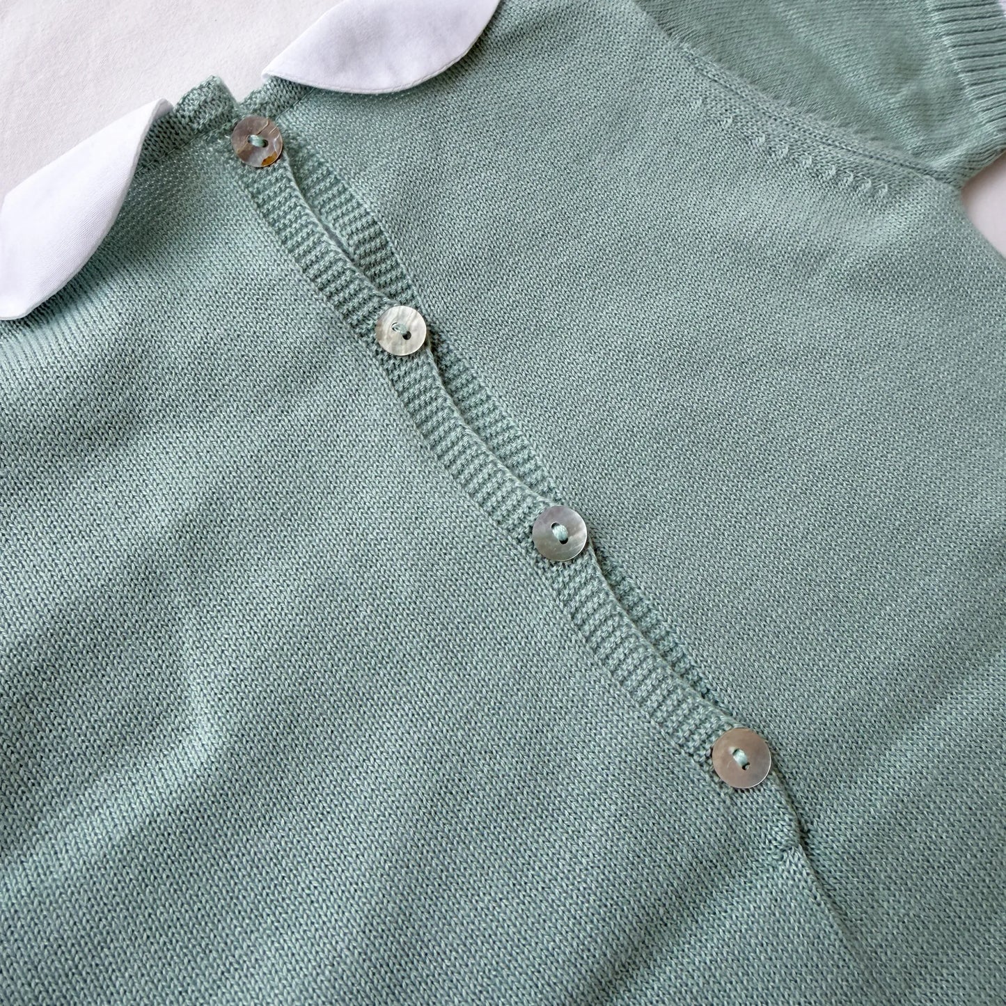 Pormenor de macacão em malha com gola Peter Pan e motivo ursinho verde