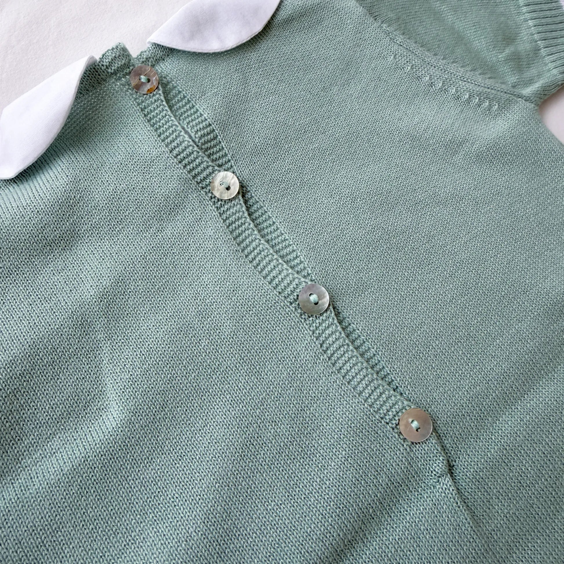 Pormenor de macacão em malha com gola Peter Pan e motivo ursinho verde