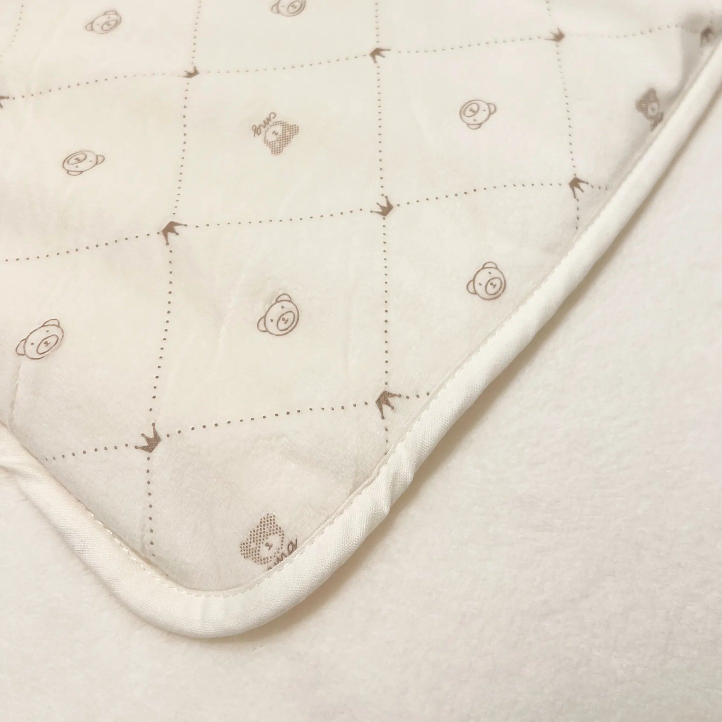 Pormenor de manta dupla face com estampado de ursinhos e losangos de um lado pérola