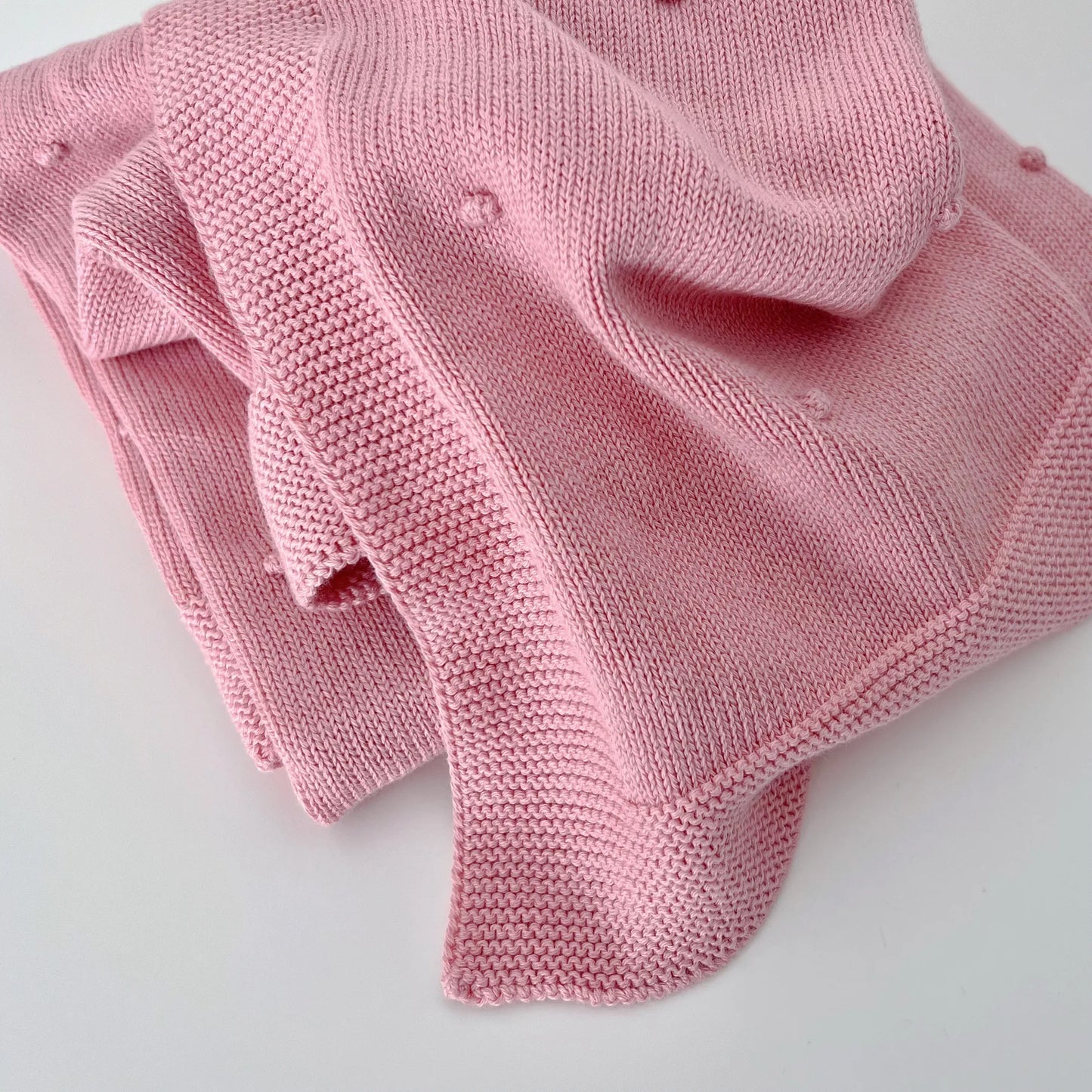 Pormenor de manta em tricot com relevo de pompons rosa