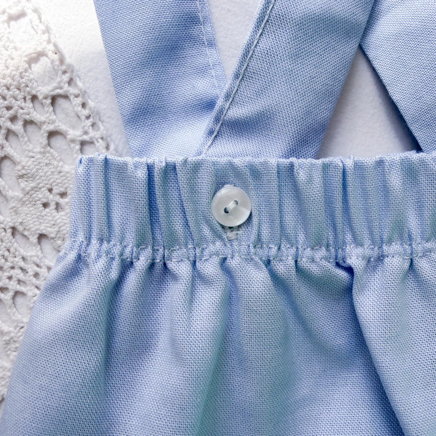 Pormenor de tapa-fraldas em tecido liso com alças azul