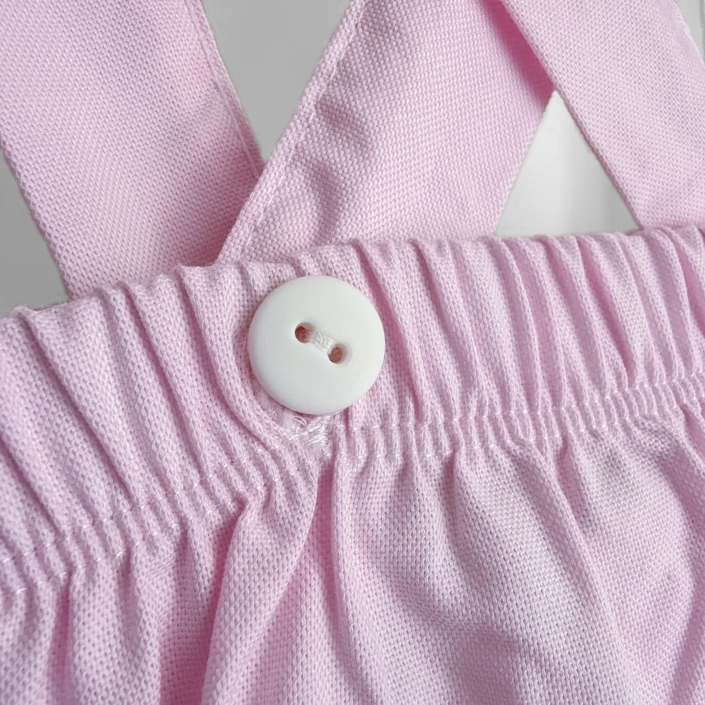 Pormenor de tapa-fraldas em tecido liso com alças rosa