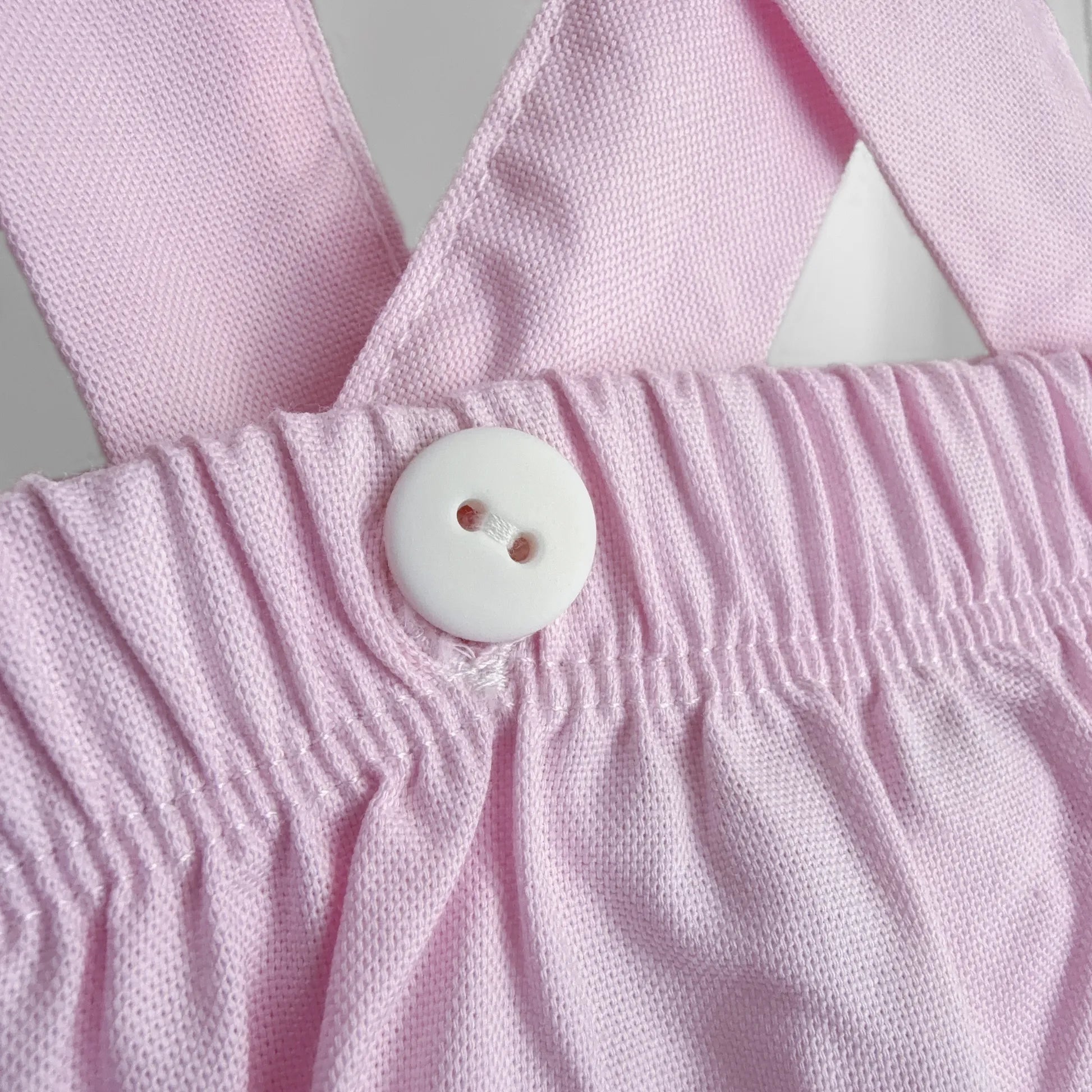 Pormenor de tapa-fraldas em tecido liso com alças rosa