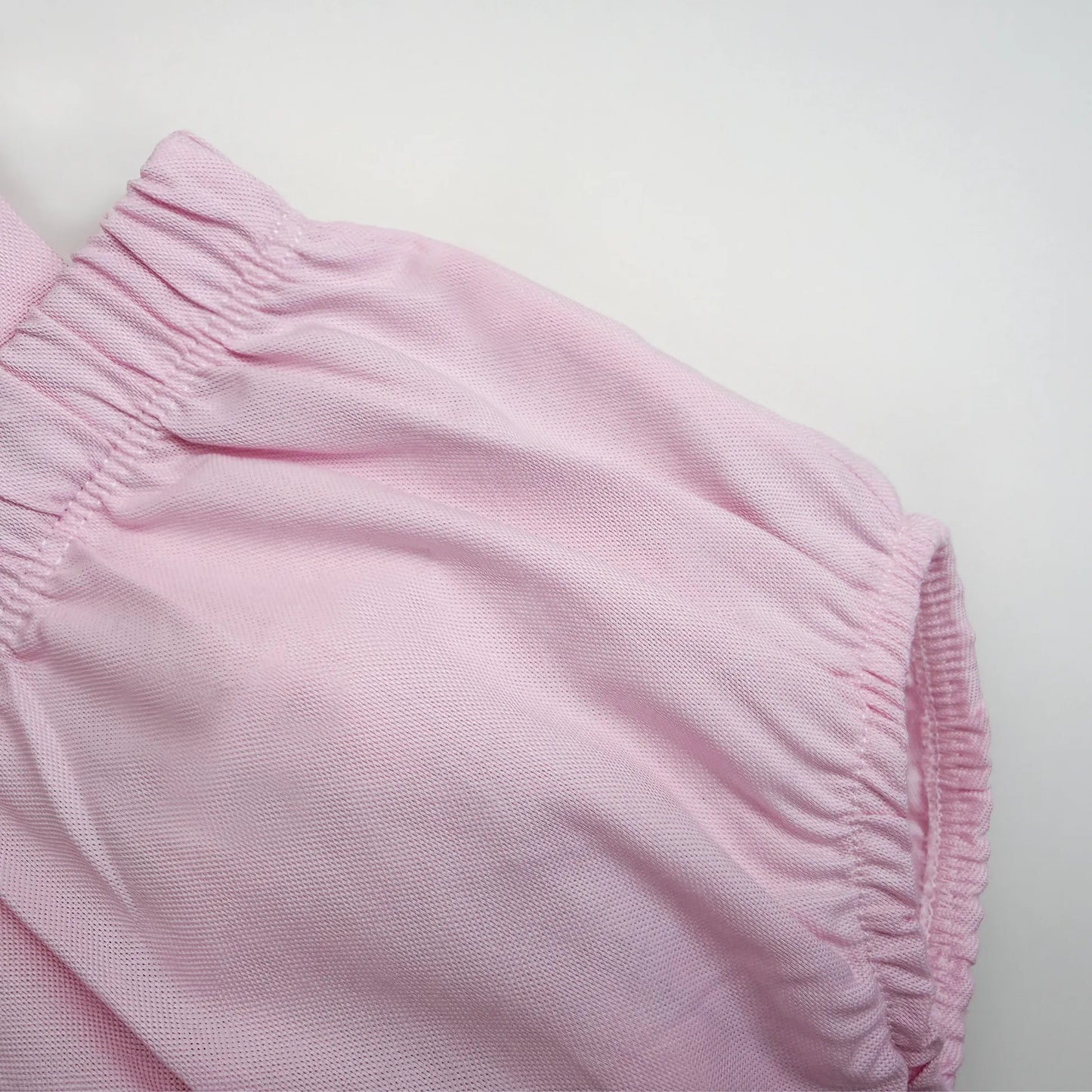 Pormenor de tapa-fraldas em tecido liso com alças rosa