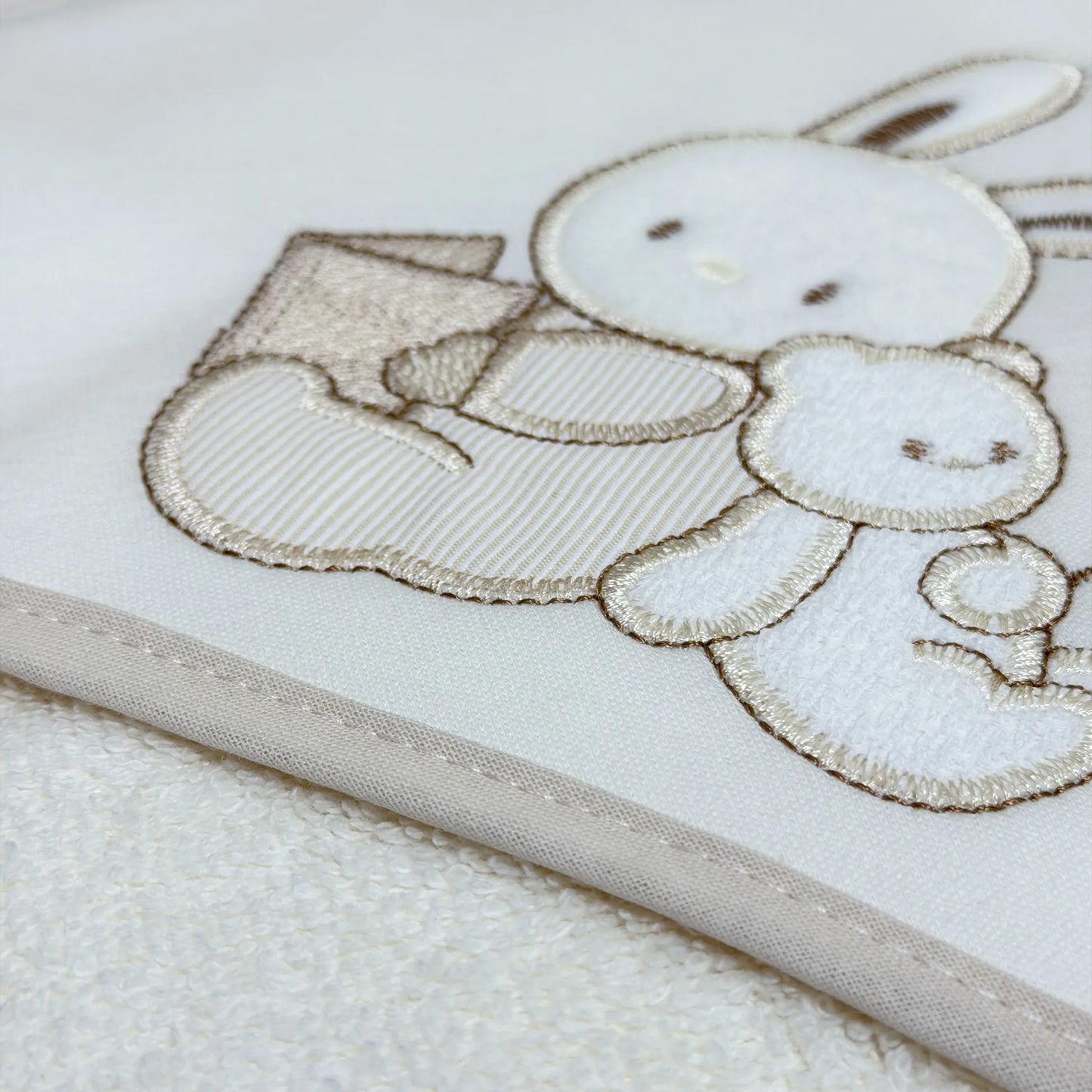 Pormenor de toalha com motivo coelhinho e ursinho com livro pérola